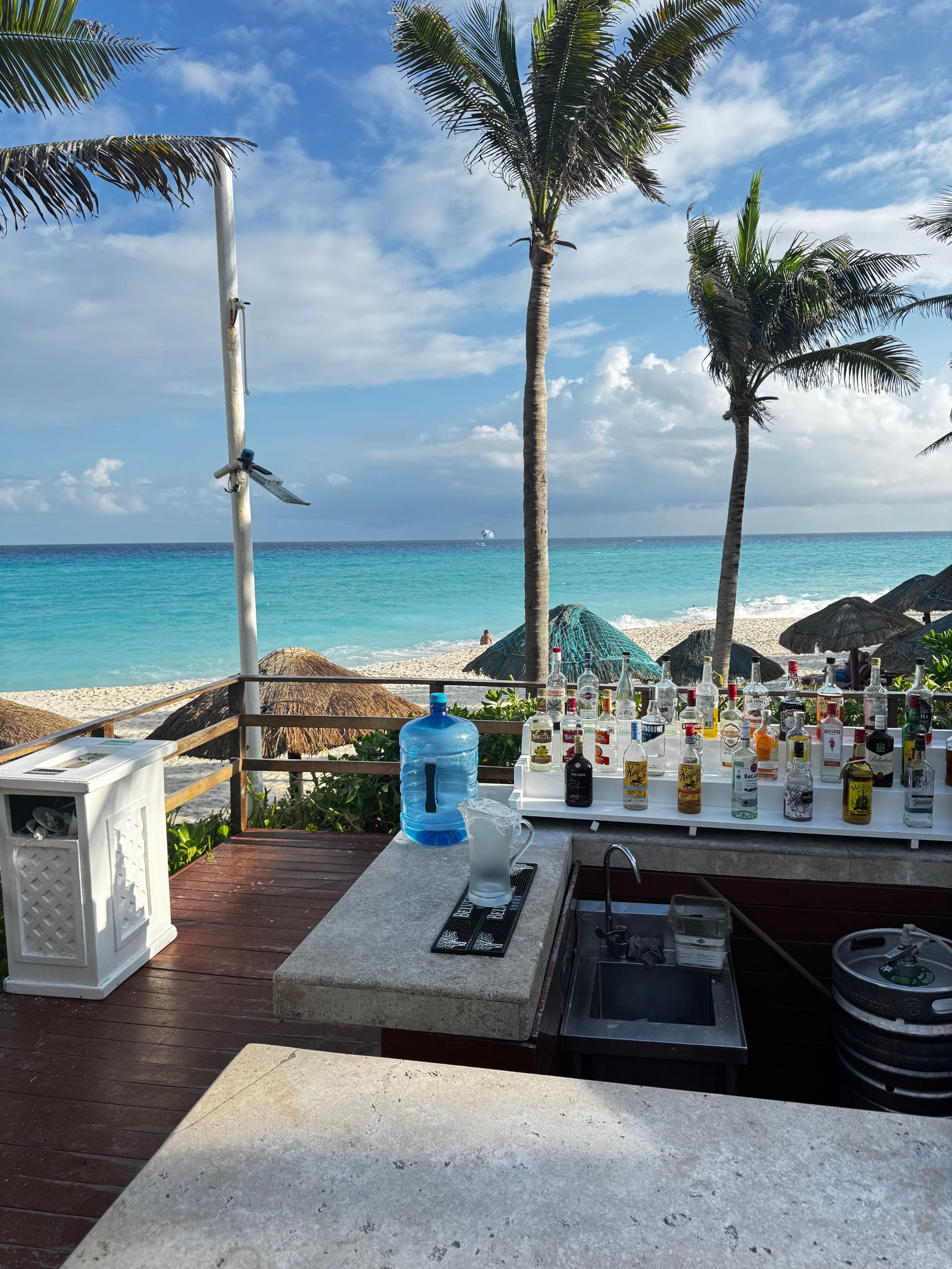 Beach bar with turquoise ocean in the background, palm trees, and clear blue sky.