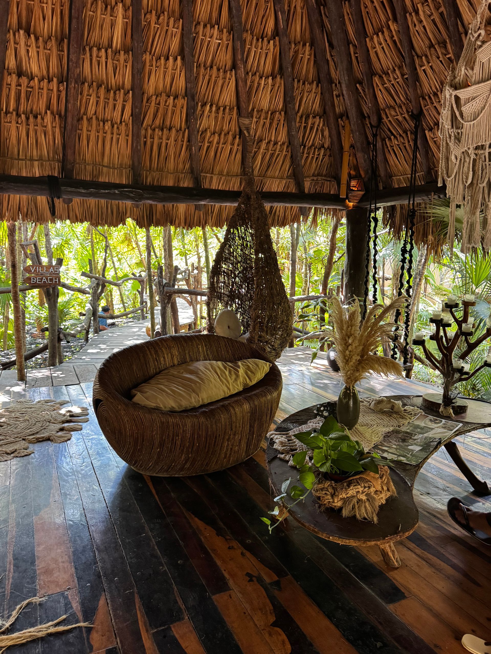 Woven seating area with a forest view, under a thatched roof in Tulum, Mexico.