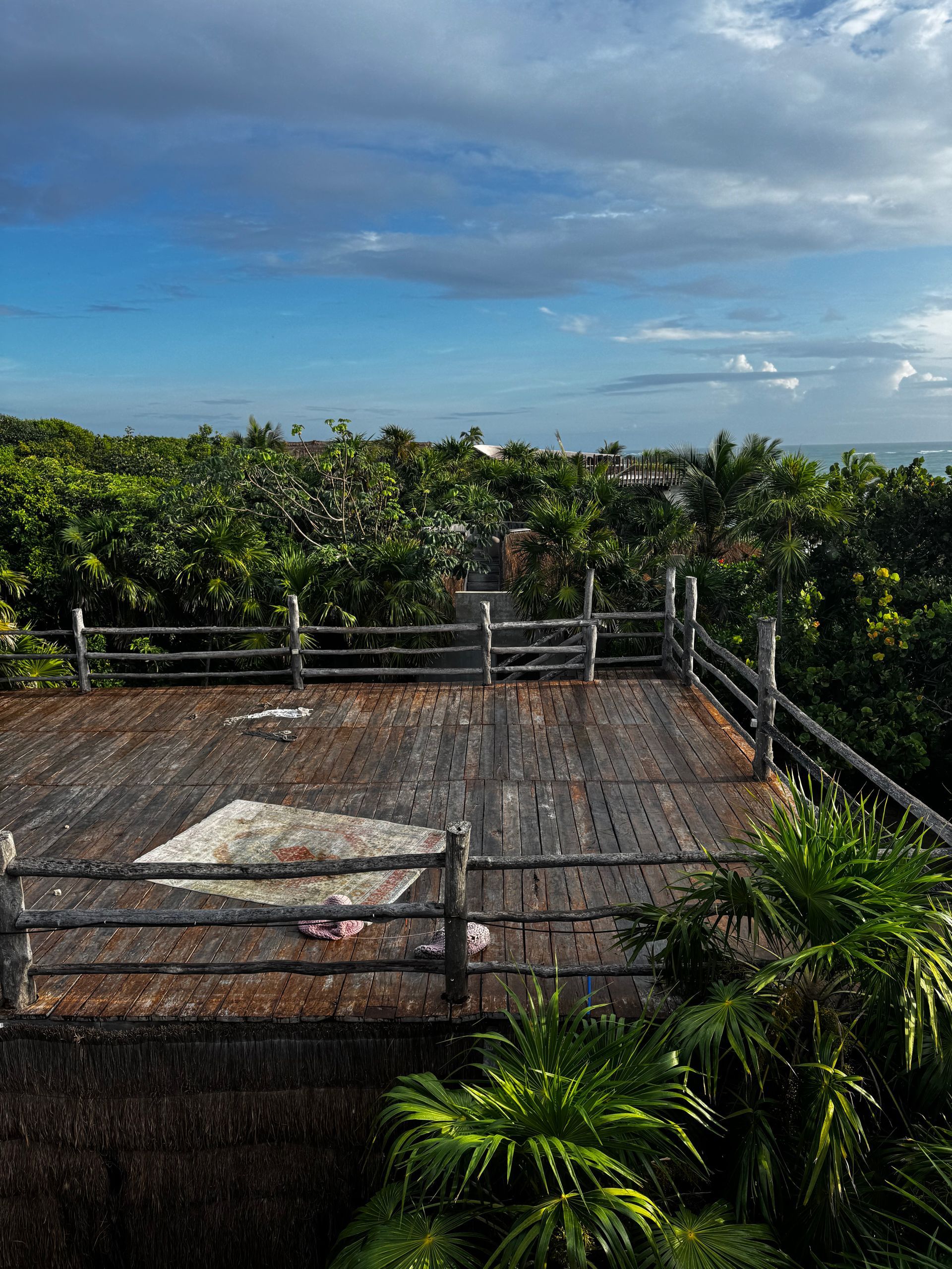 A wooden deck with a fence and trees in the background at Papaya Playa Project hotel in Tulum, Mexico.