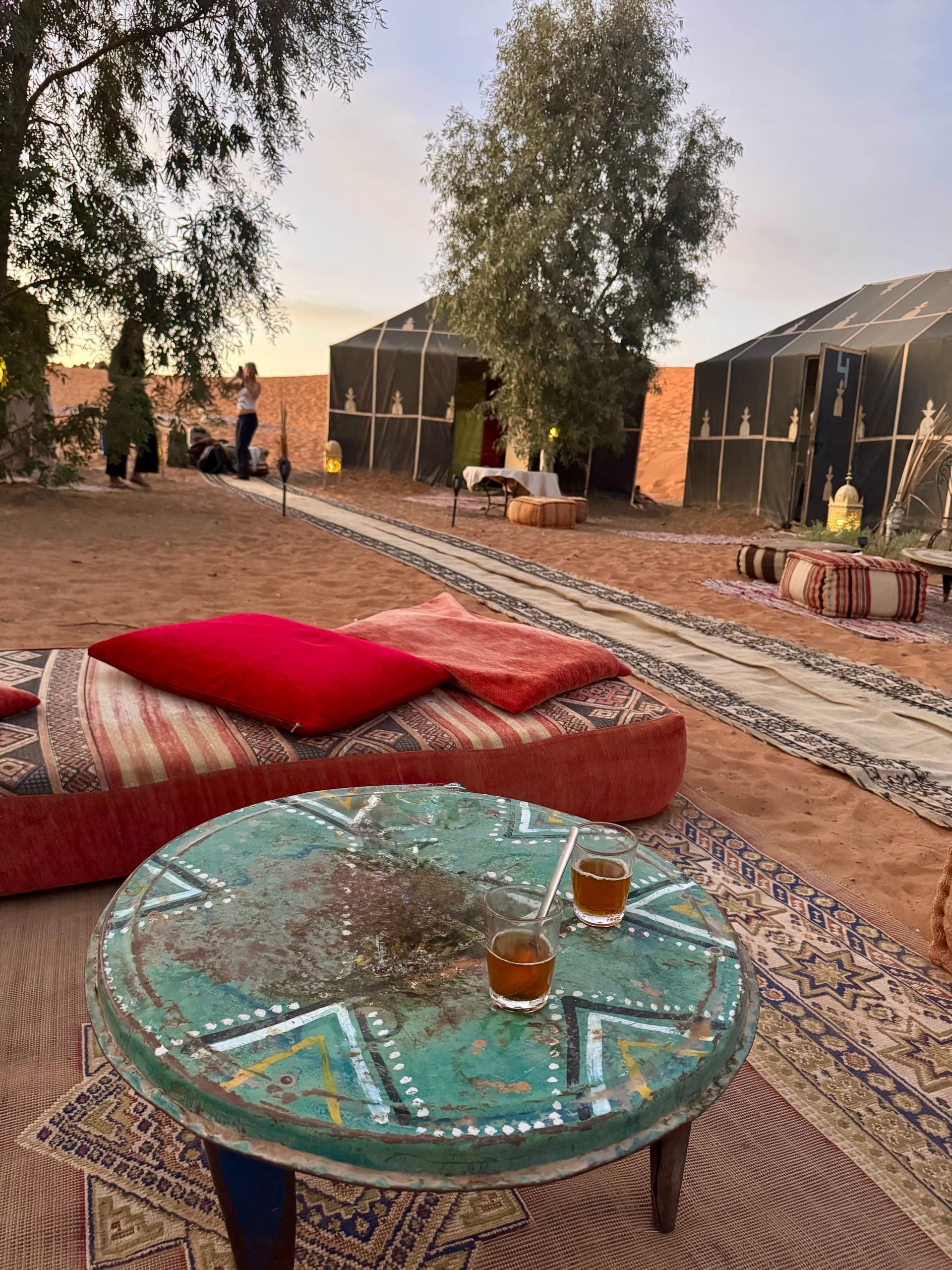 Desert camp scene with tents, seating, and tea on a round table.