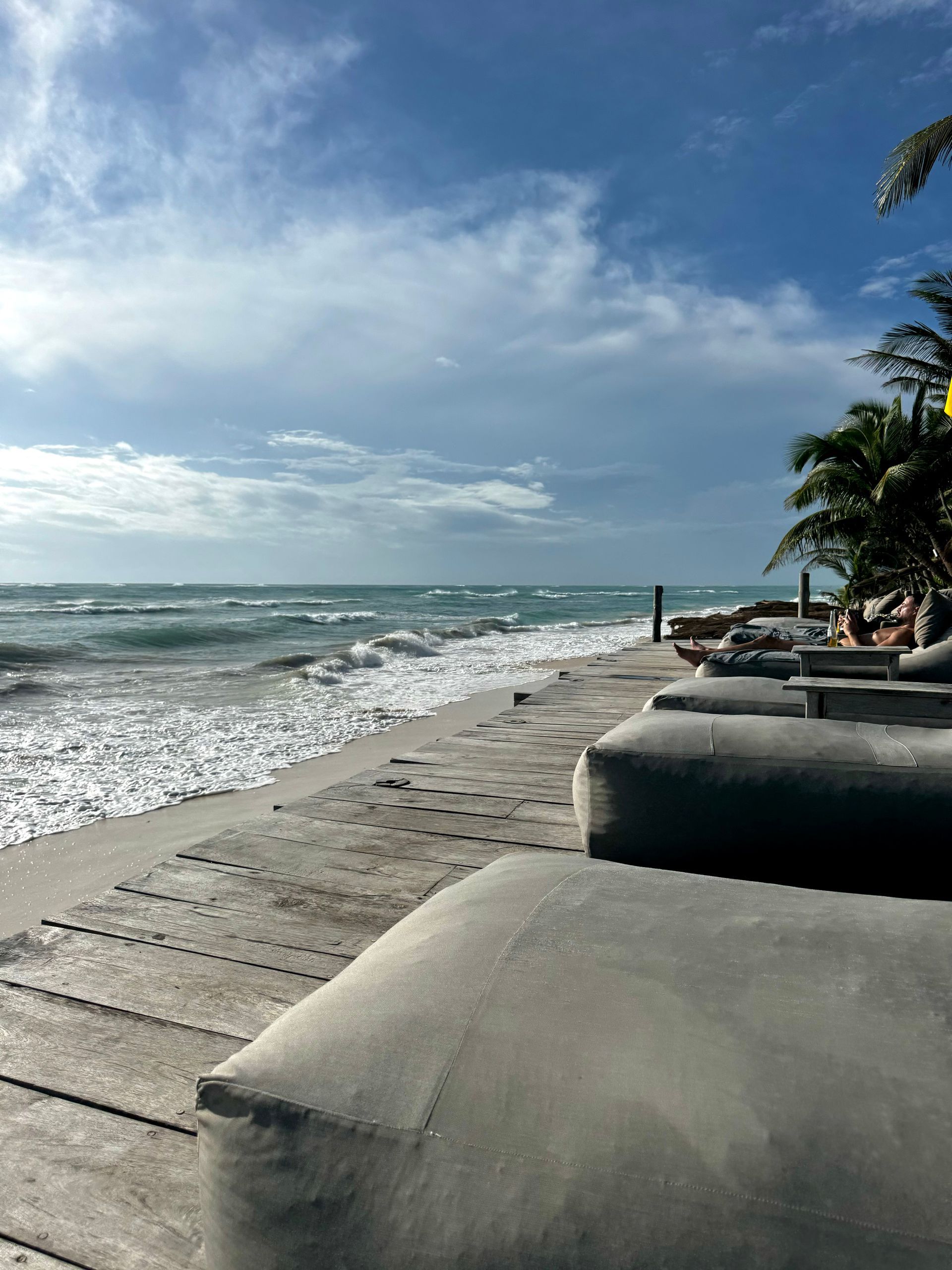 Beach scene: Gray beanbag chairs on a sandy shore facing the ocean under a blue sky.