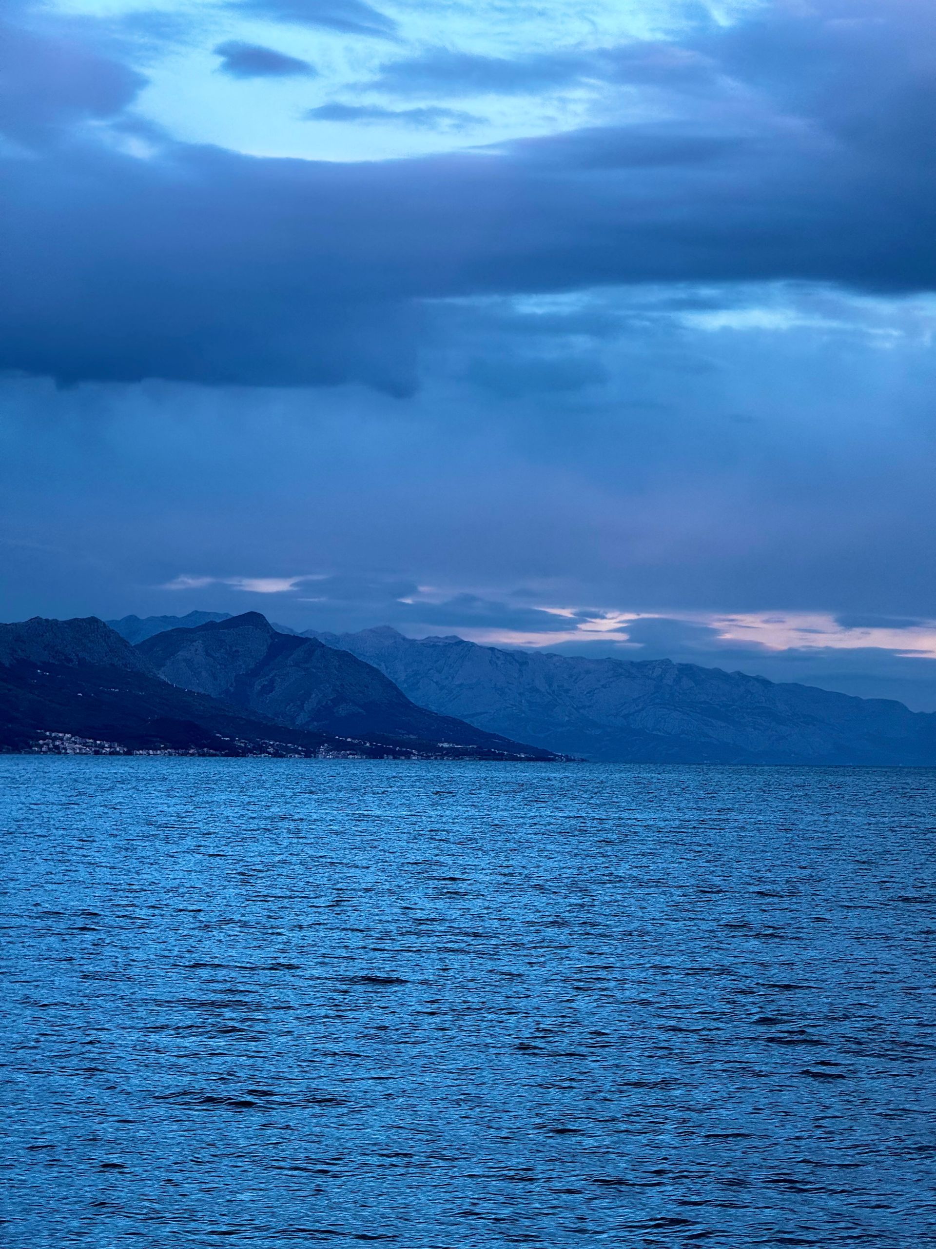 Ocean with mountains under a cloudy, blue sky.