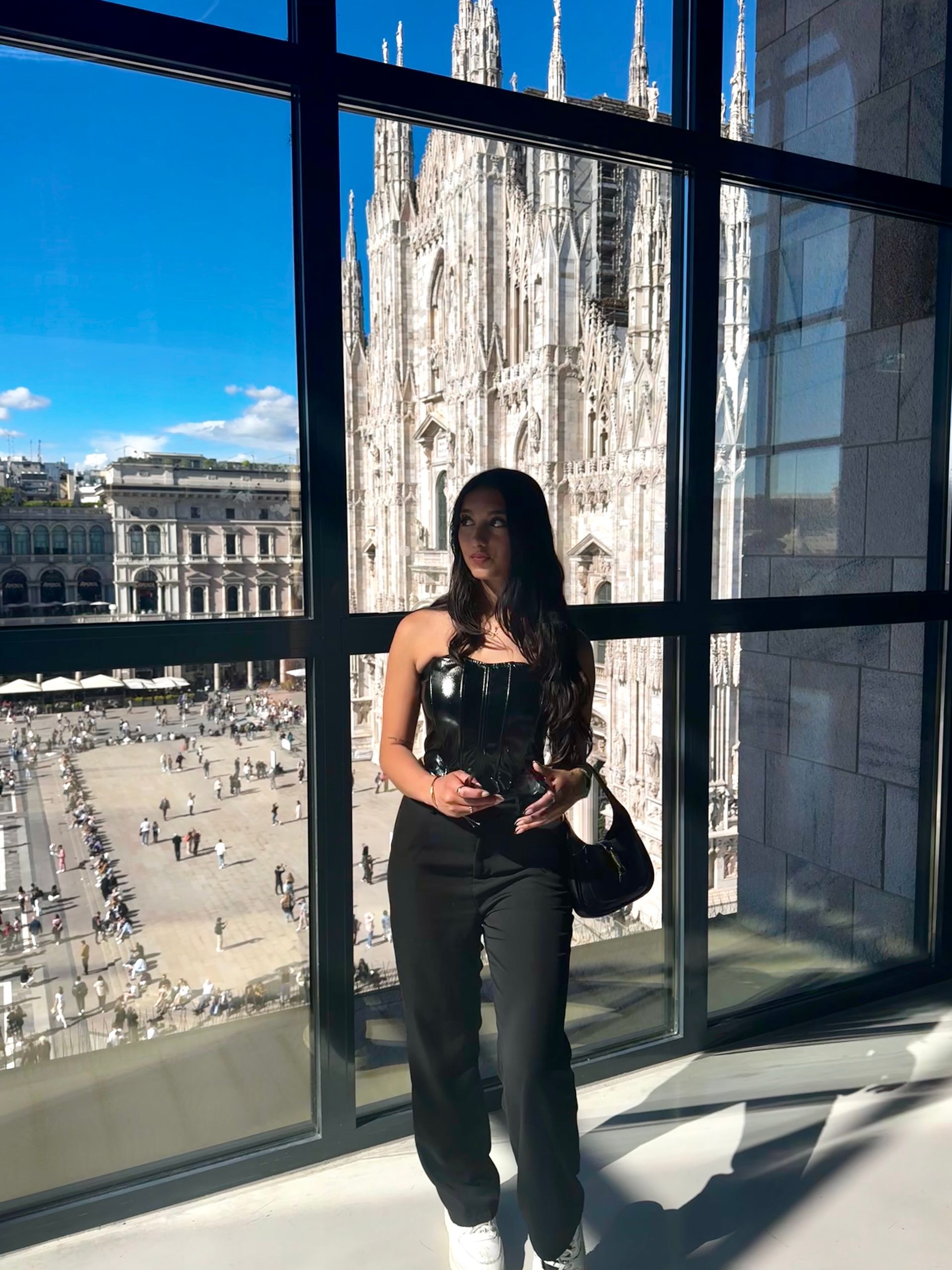 Woman in black outfit stands before a window overlooking Milan Cathedral and square.