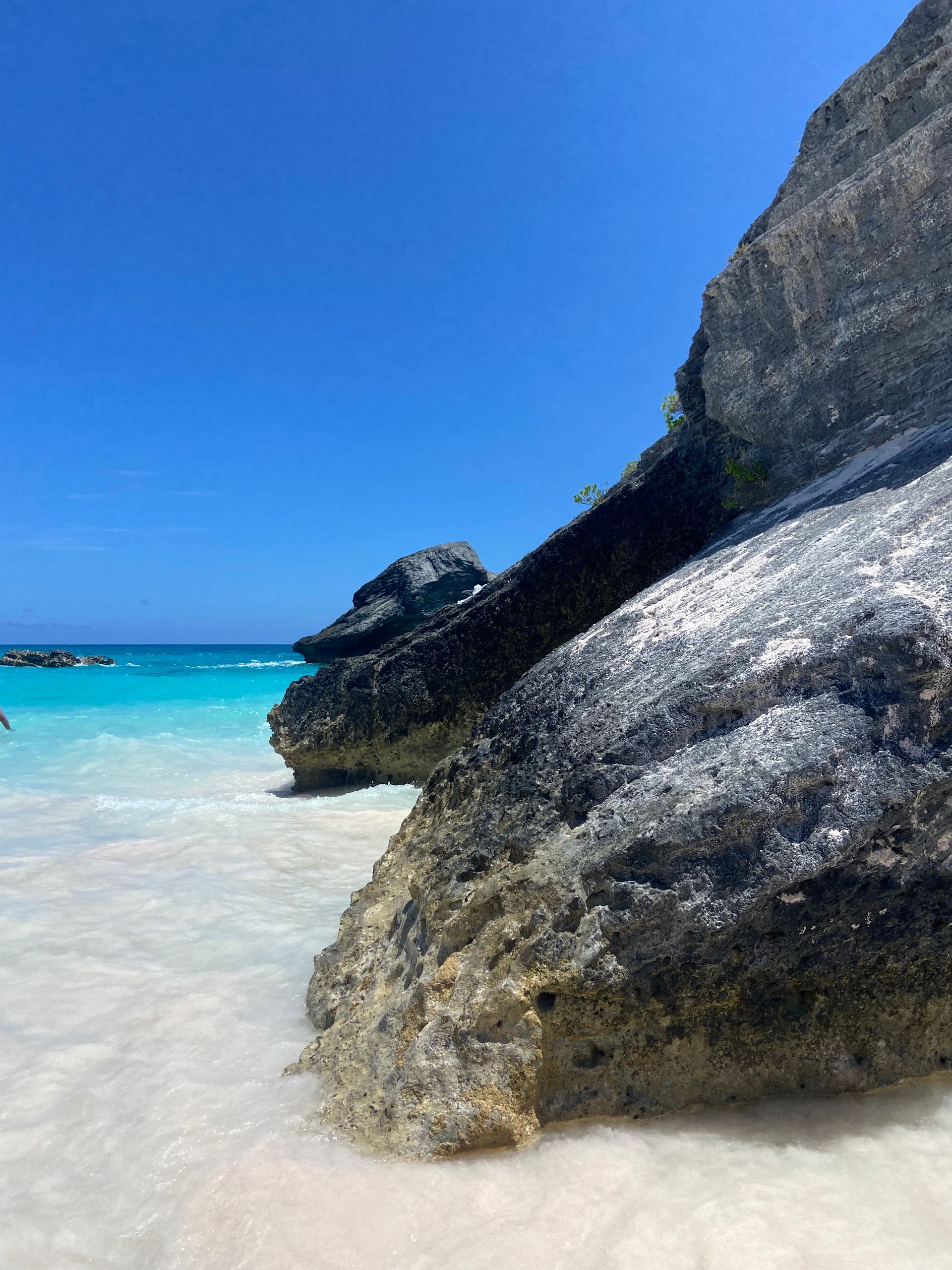 Blue sky over a beach with light blue water, white sand, and large gray rocks.