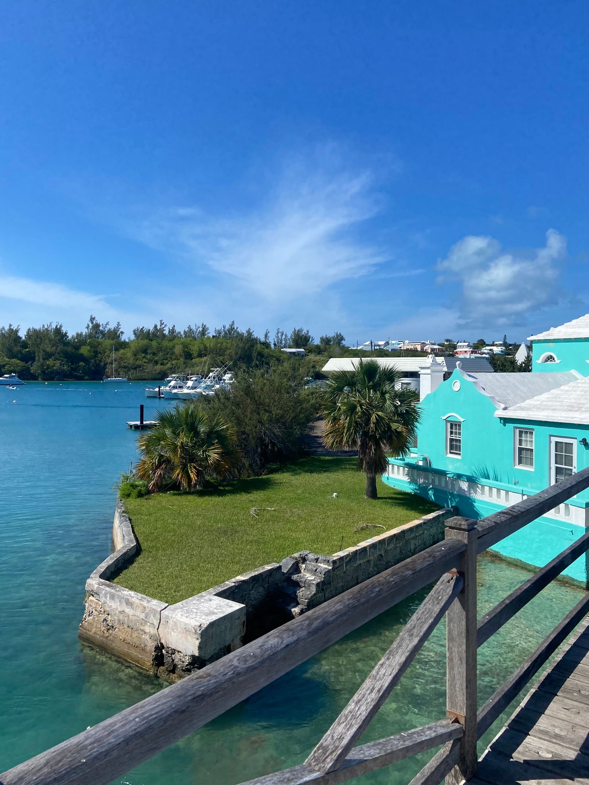 Turquoise building and water by a wooden railing under a bright blue sky.