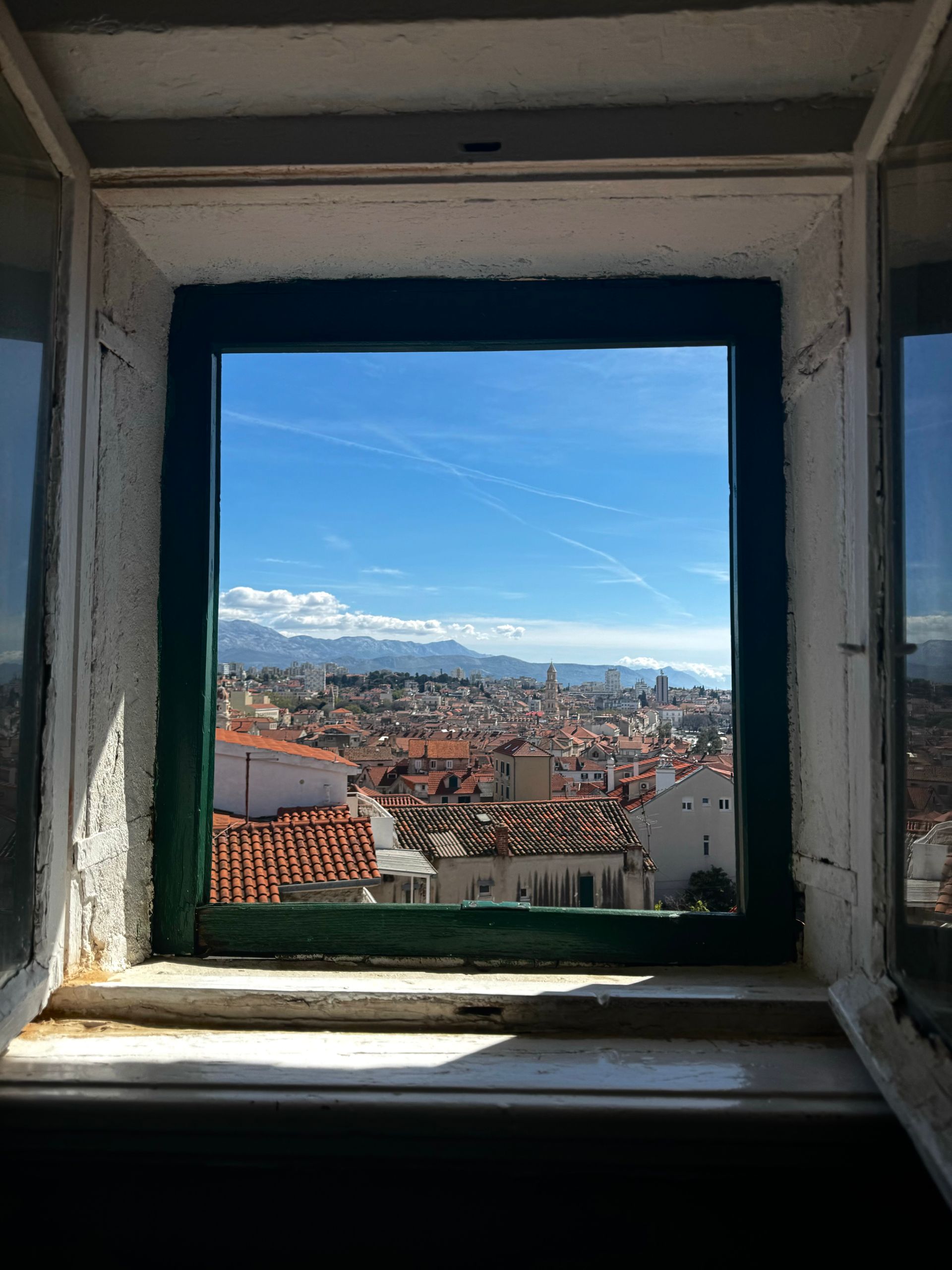 View from a window overlooking a city with red rooftops and blue sky.
