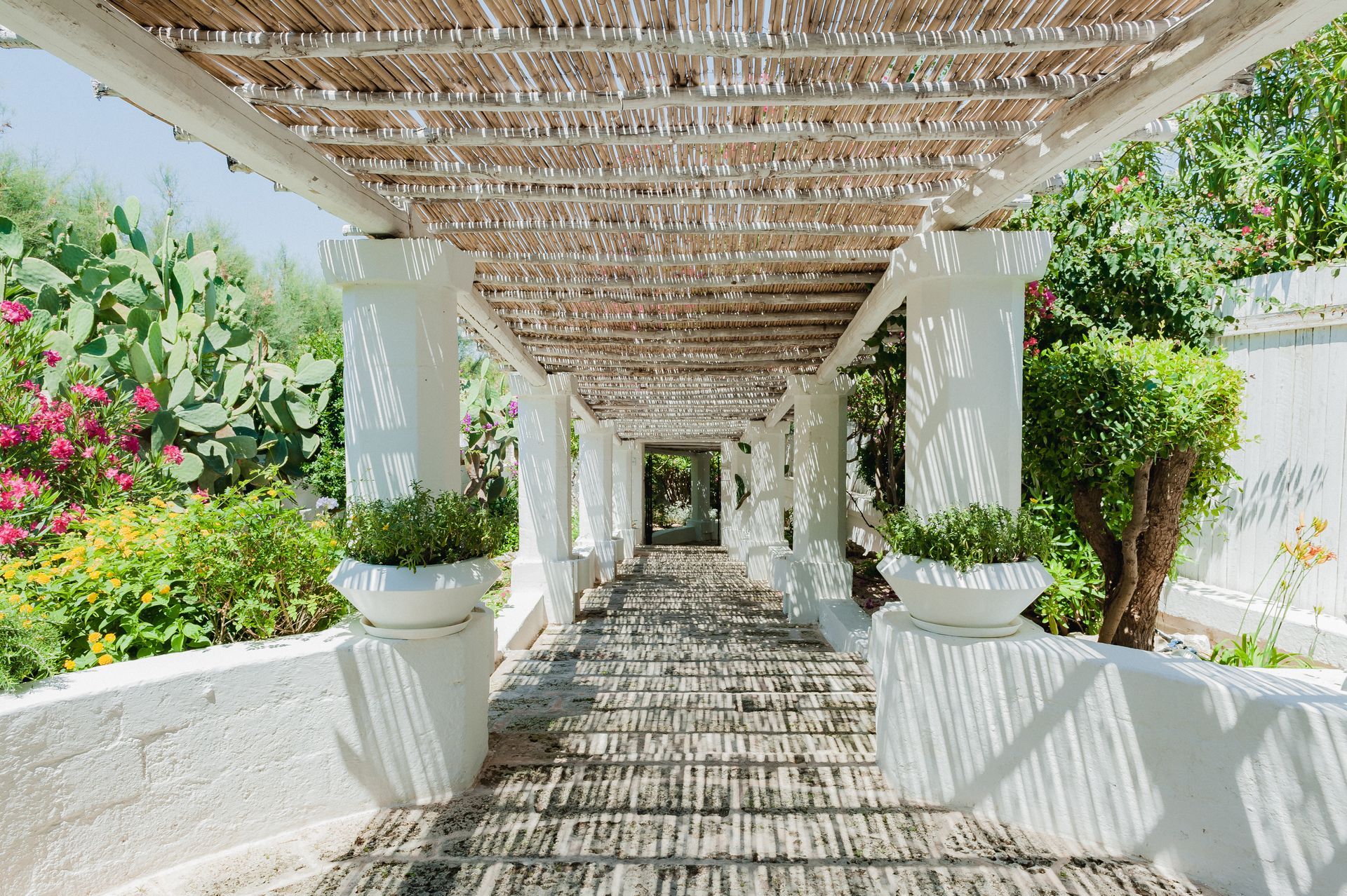 A long walkway with a wooden roof and potted plants at La Peschiera Hotel in Puglia, Italy.