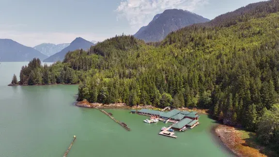 An aerial view of a marina in the middle of a lake surrounded by mountains in the Great Bear Rainforest.