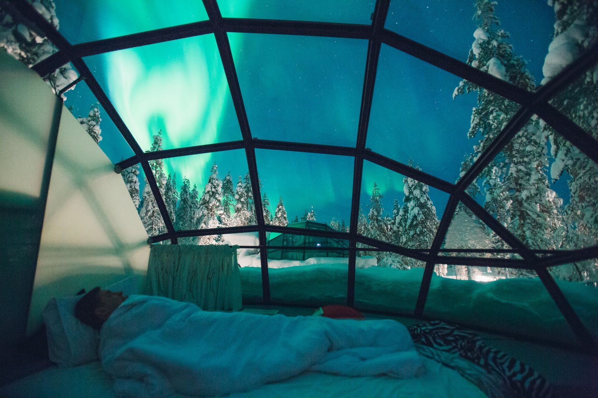 A person is sleeping in a glass igloo with the aurora borealis in the background in finland.