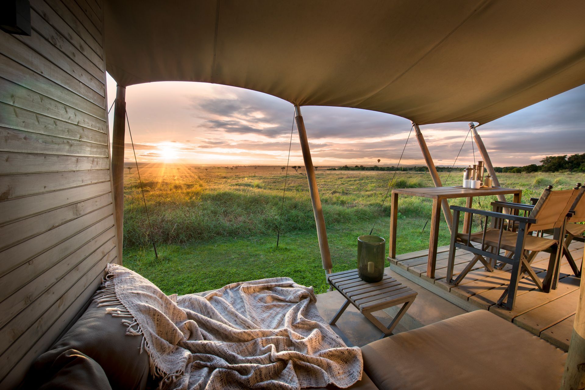 A view of a sunset from a tent with a table and chairs at a camp in Africa.