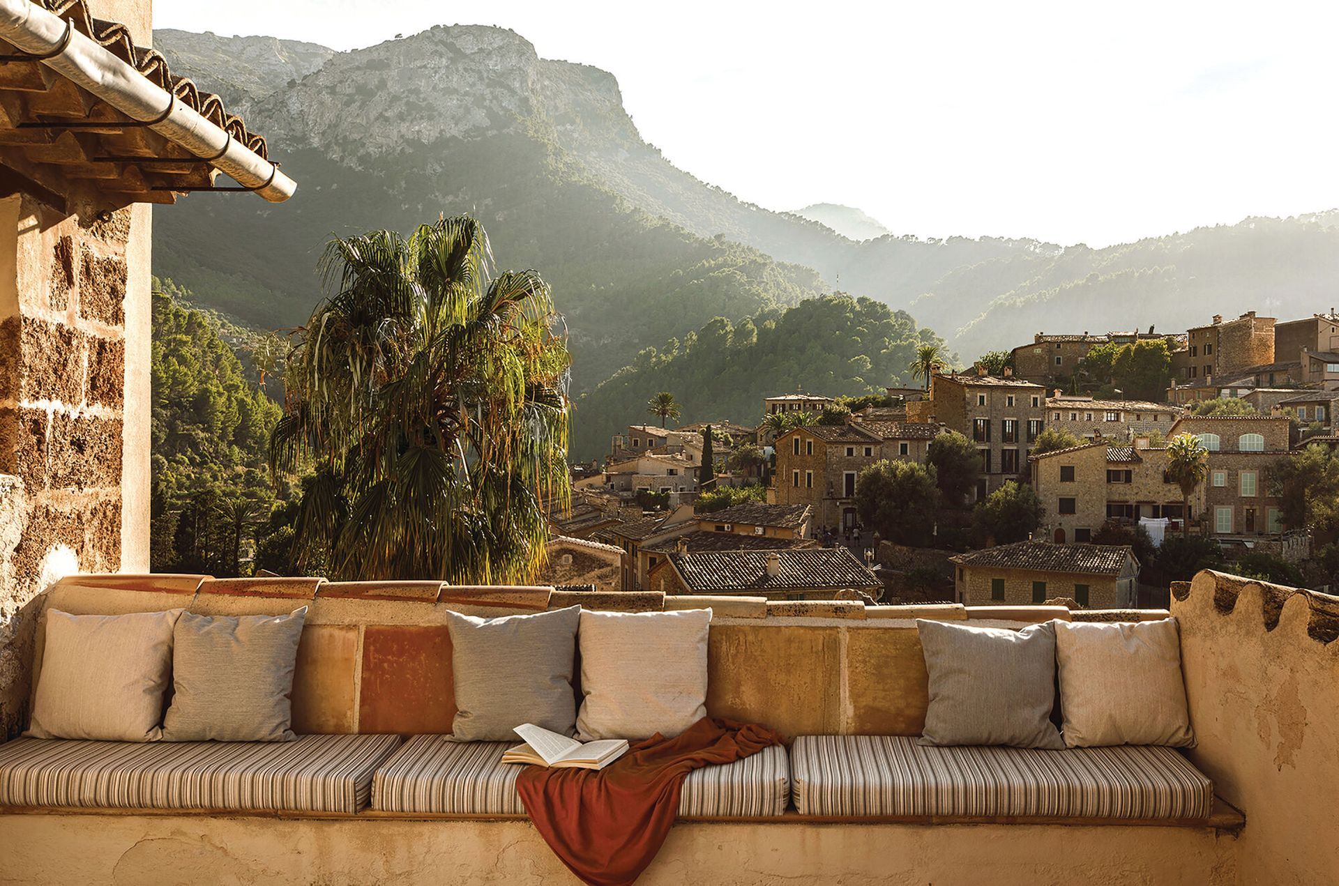 A couch with pillows and a book on it with a view of the mountains in Mallorca, Spain at the Belmond hotel. 