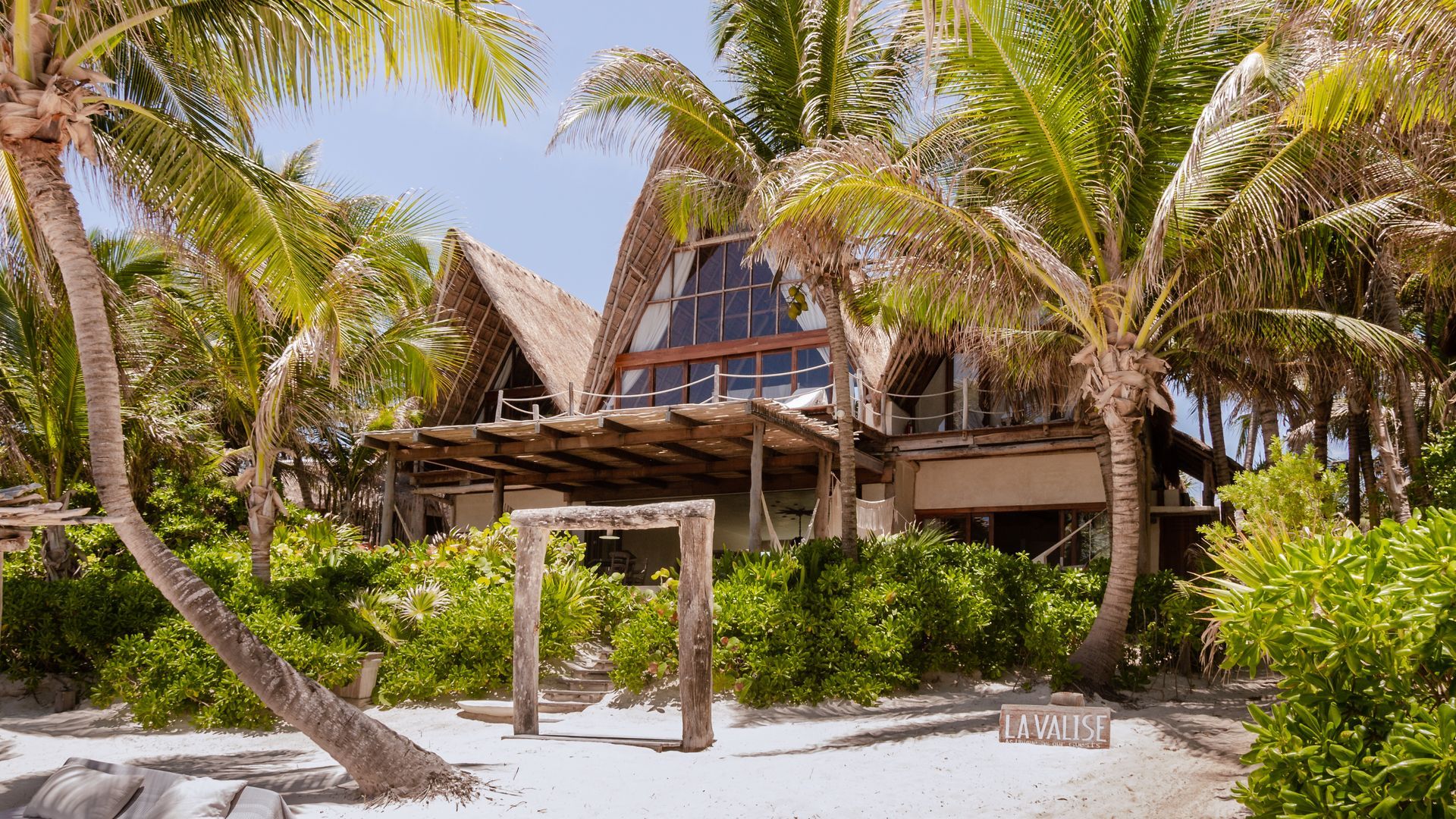 A thatched house is surrounded by palm trees on a tropical beach at La Valise Tulum Hotel in Mexico.