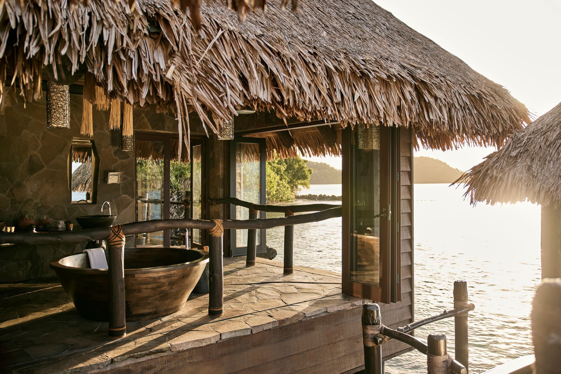 A villa with a thatched roof overlooking a body of water in Fiji. 