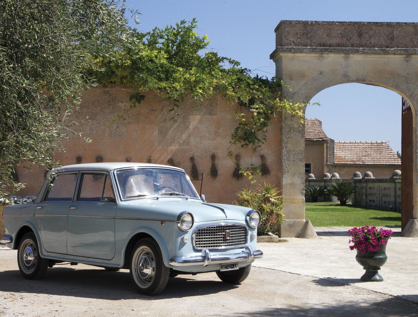 A blue car is parked in front of a stone archway at Naturalis Bio Resort & Spa in Puglia, Italy.