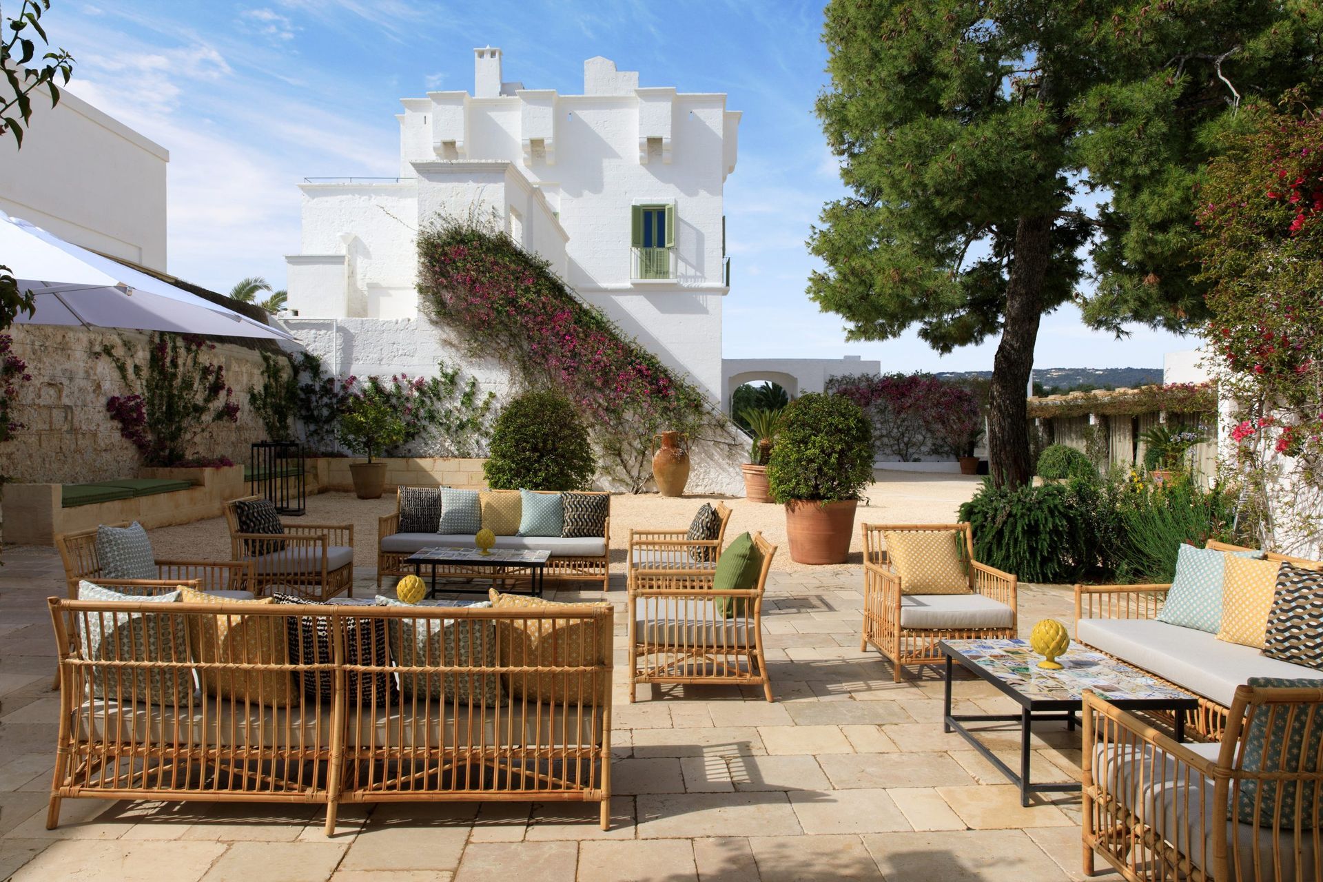 A patio with furniture and umbrellas in front of a white building in Puglia, Italy at Rocco Forte Hotel.
