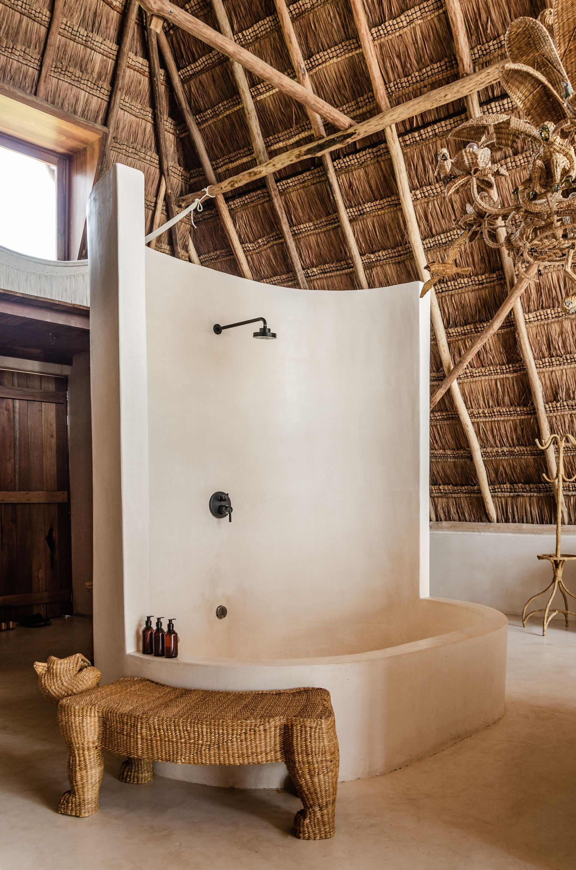 A bathroom with a bathtub and a shower with a thatched roof at La Valise Tulum hotel in Mexico.