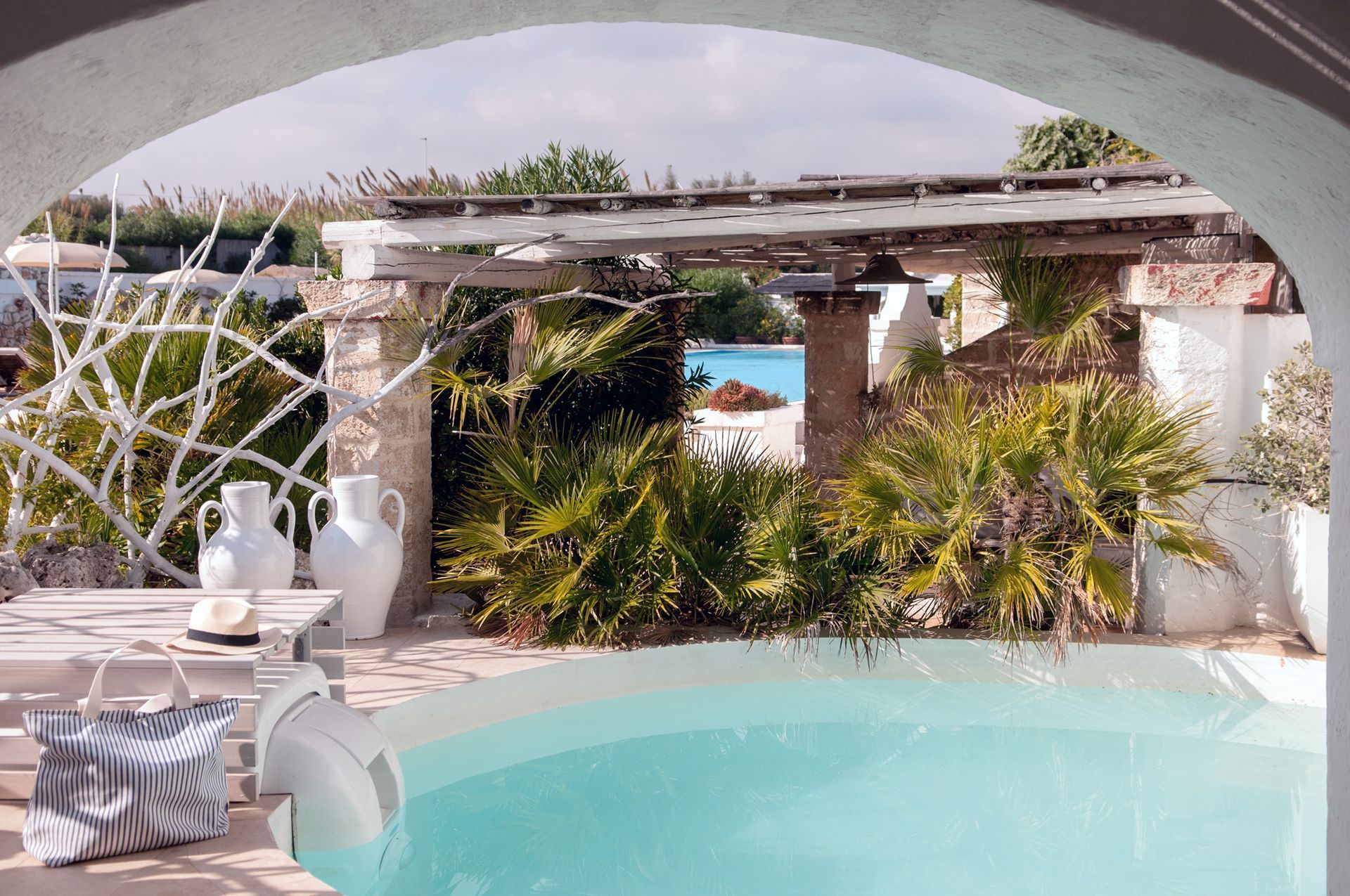 A large swimming pool is surrounded by plants and a pergola at La Peschiera Hotel in Puglia, Italy.