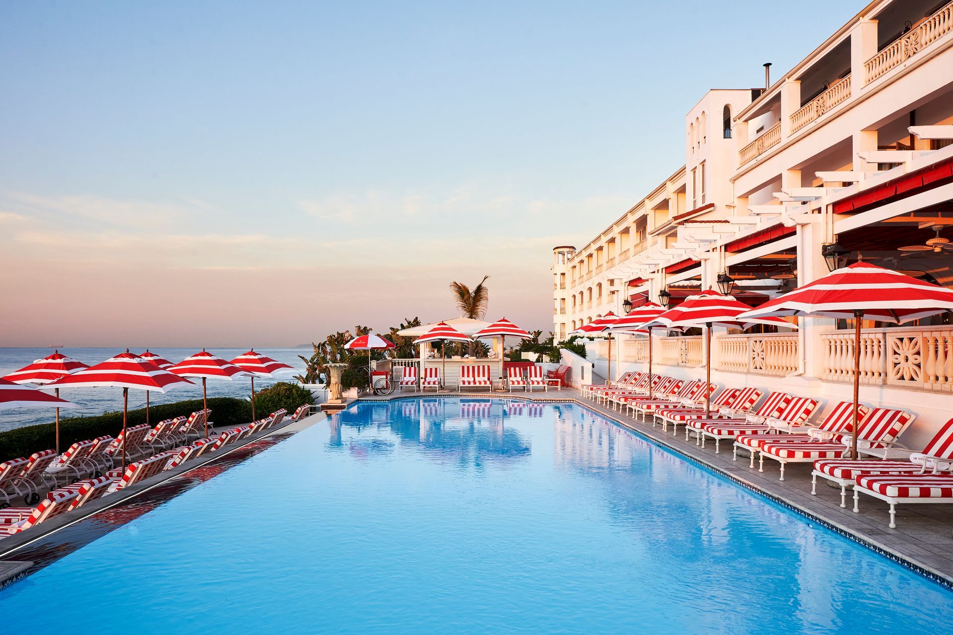 A large swimming pool surrounded by chairs and umbrellas at the South Africa Red Carnation Hotel.