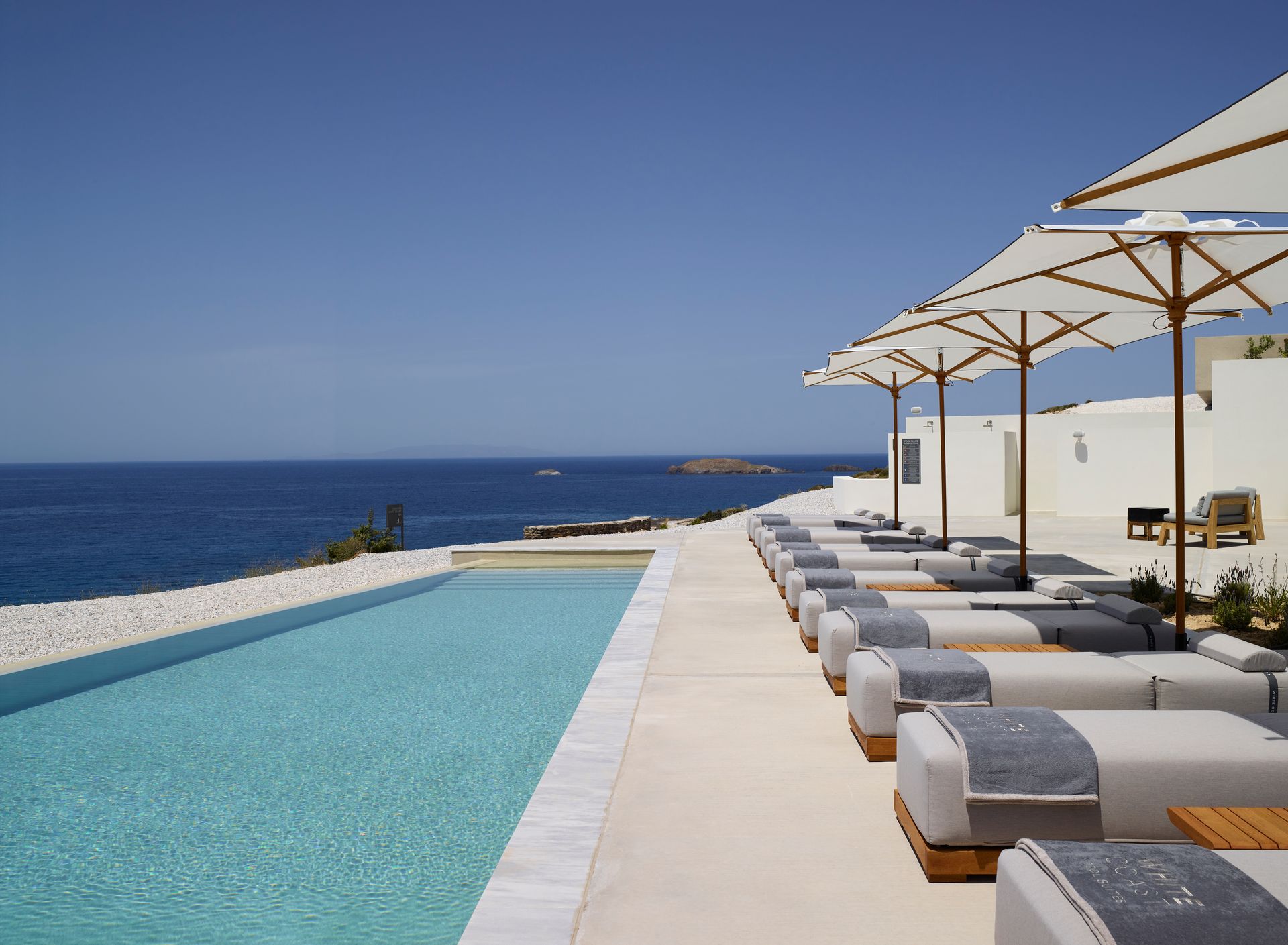 A swimming pool surrounded by lounge chairs overlooking the ocean at Domes White Coast Hotel in Milos, Greece.