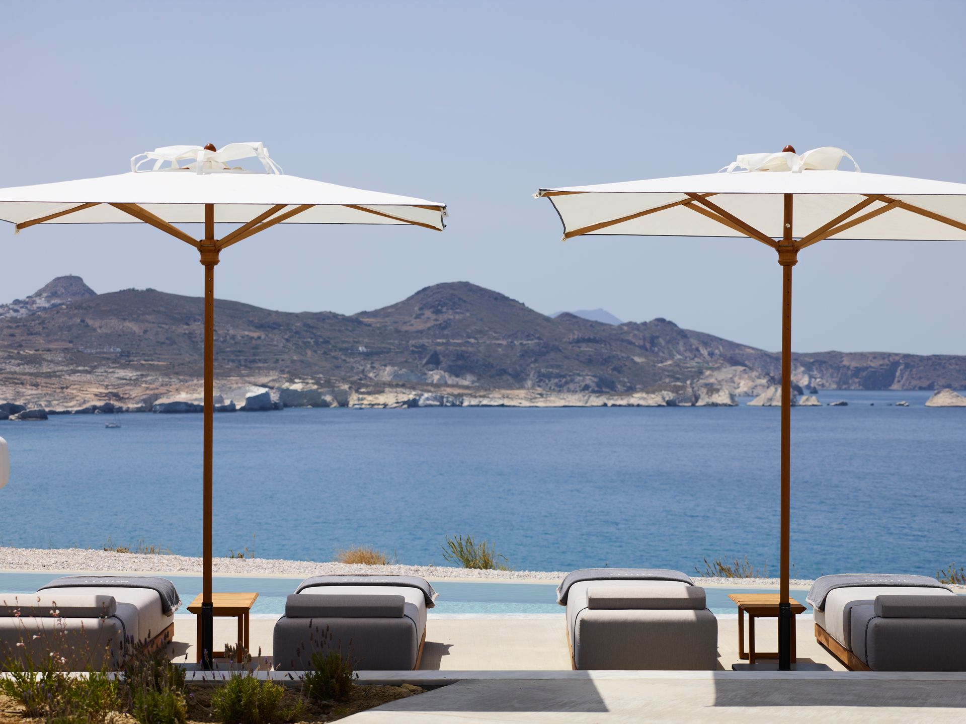 Two umbrellas are sitting next to a pool overlooking the ocean at Domes White Coast Hotel in Milos, Greece.