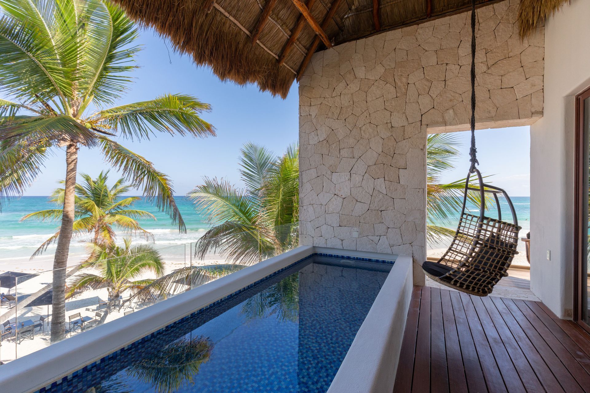 A swimming pool with a chair hanging over it and a view of the ocean at TAGO Tulum Hotel in Mexico.