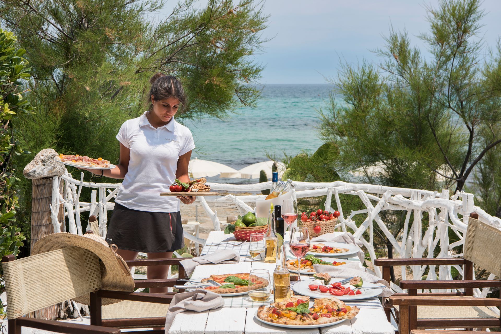 A woman is serving pizza at a table with a view of the ocean at Il Melograno Hotel in Puglia, Italy.