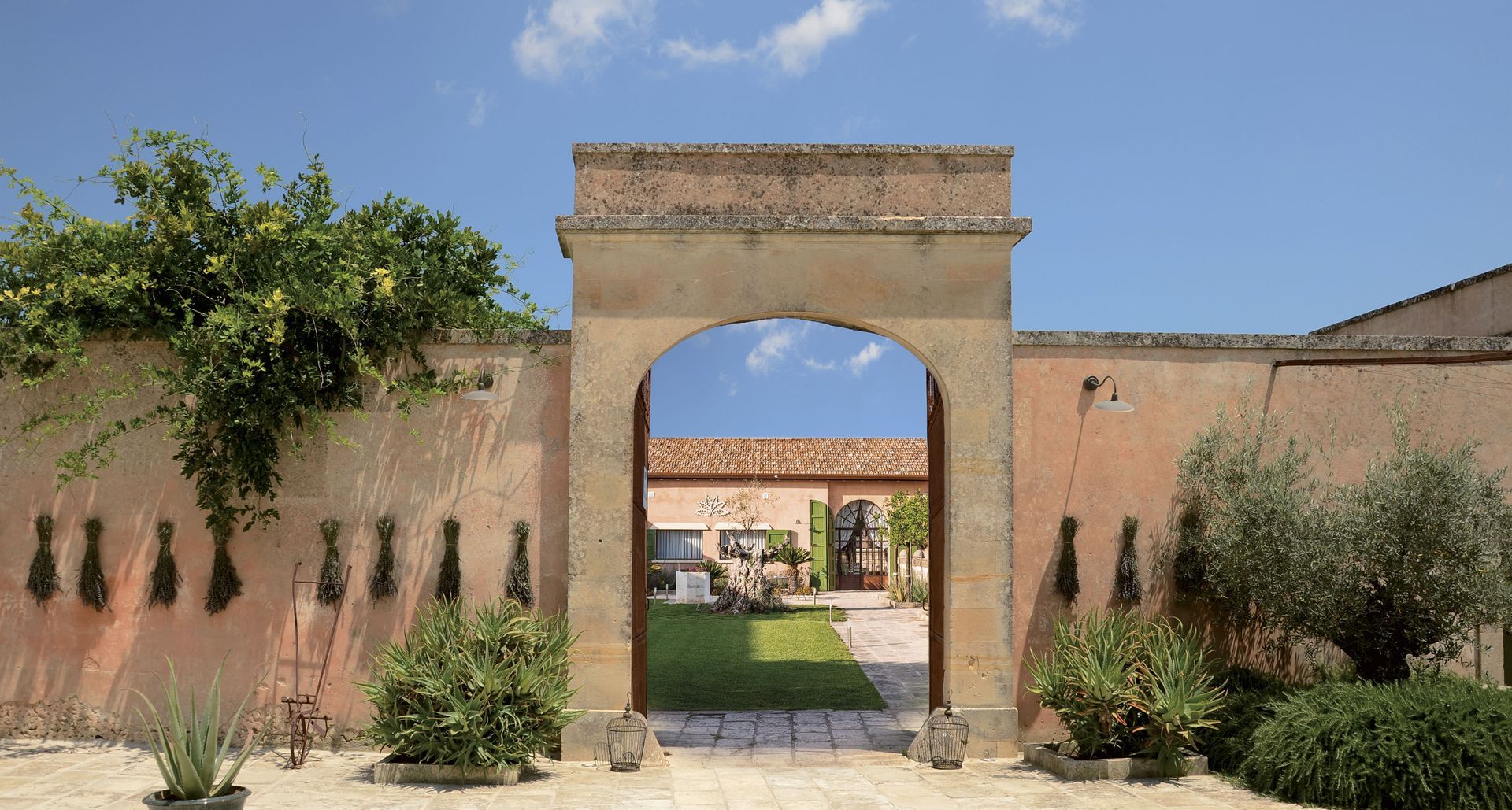 A stone archway leading to a house with a blue sky in the background at Naturalis Bio Resort & Spa in Puglia, Italy.