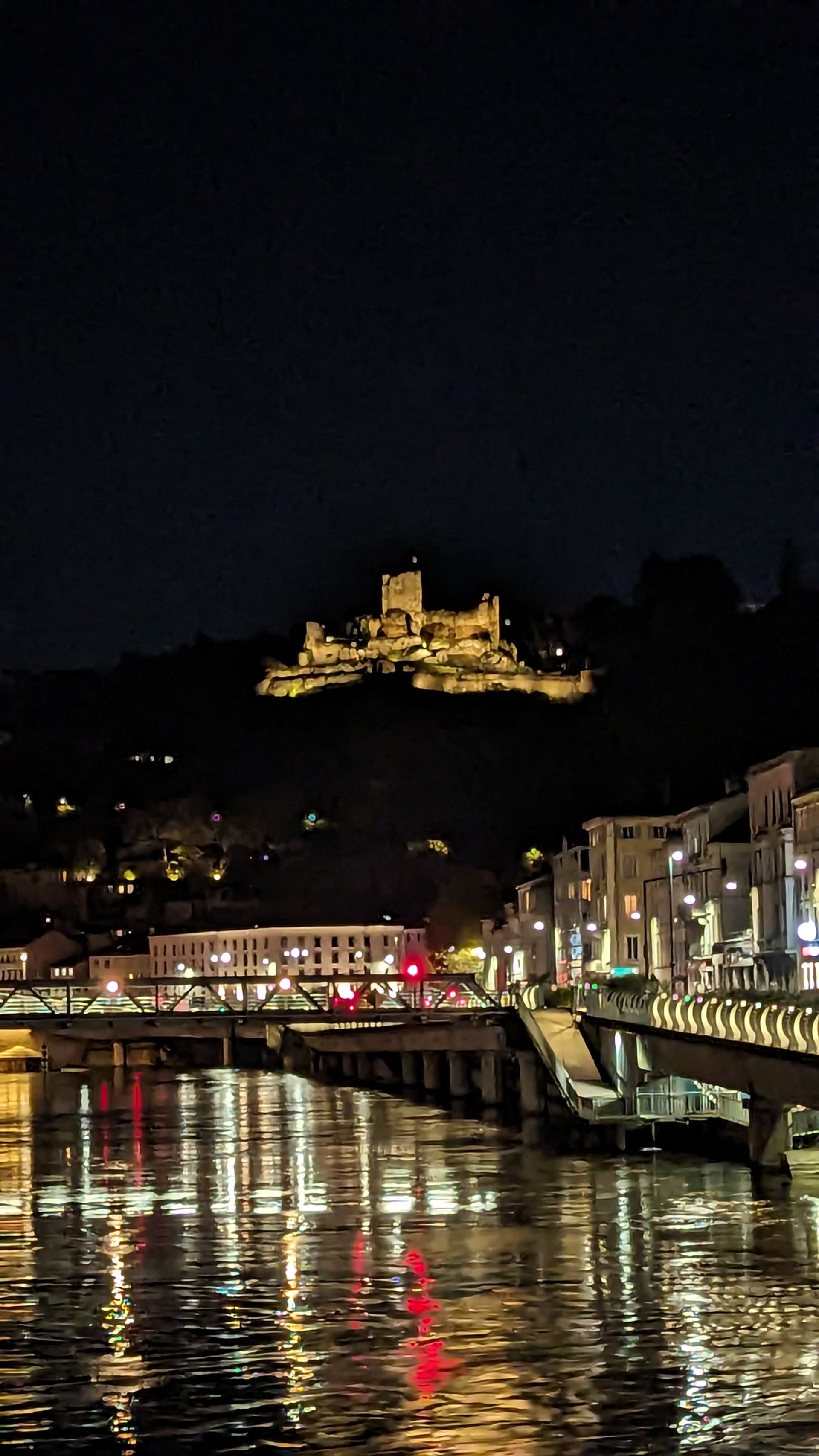Nighttime view of a river reflecting city lights and a lit castle on a hill.
