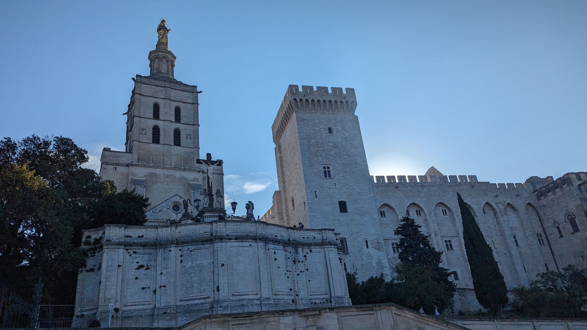 Medieval Palais des Papes in Avignon, France, under a clear blue sky. Stone facade with tall tower.