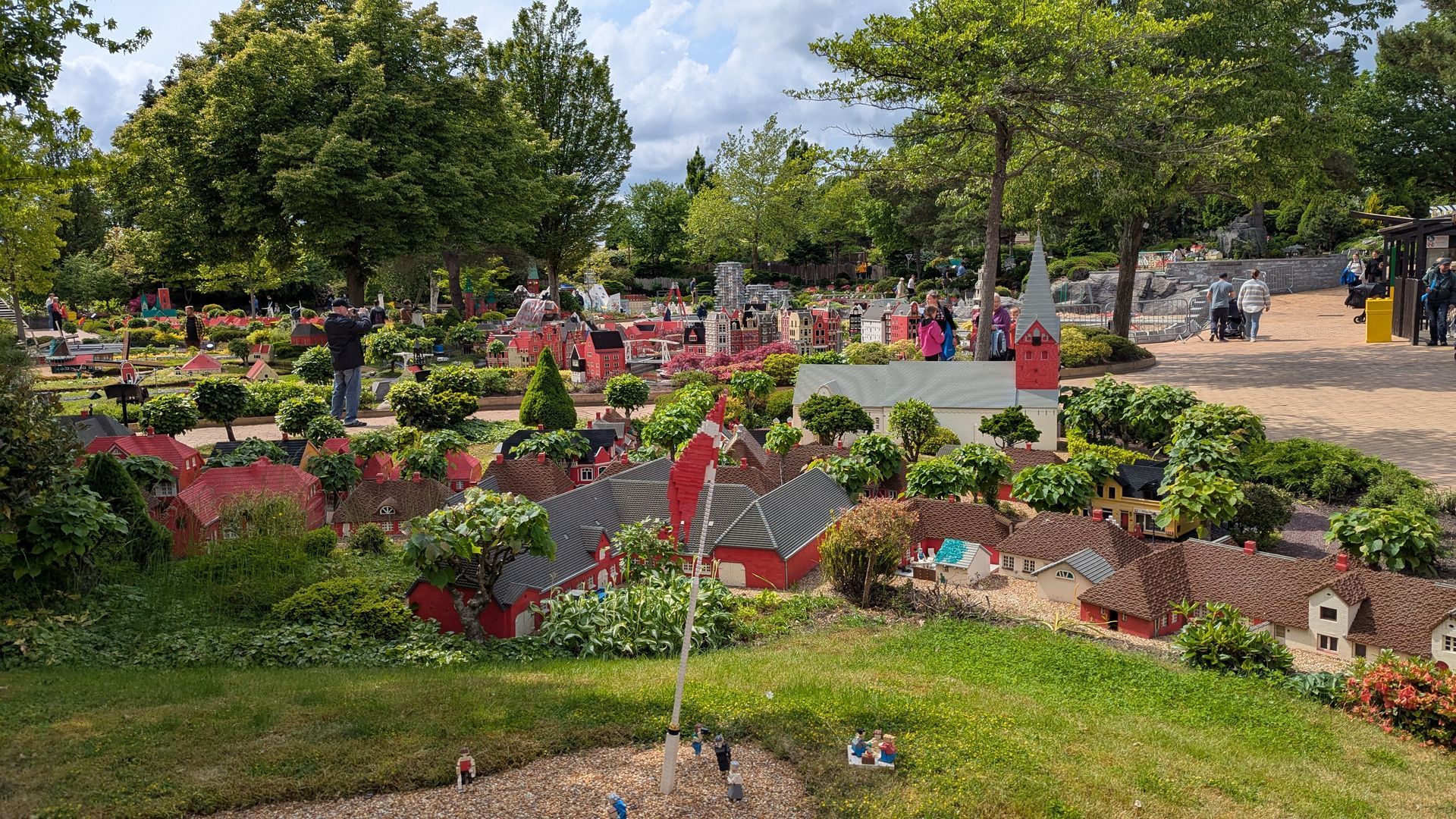 Miniature townscape in park setting with greenery and people. Buildings have red roofs.