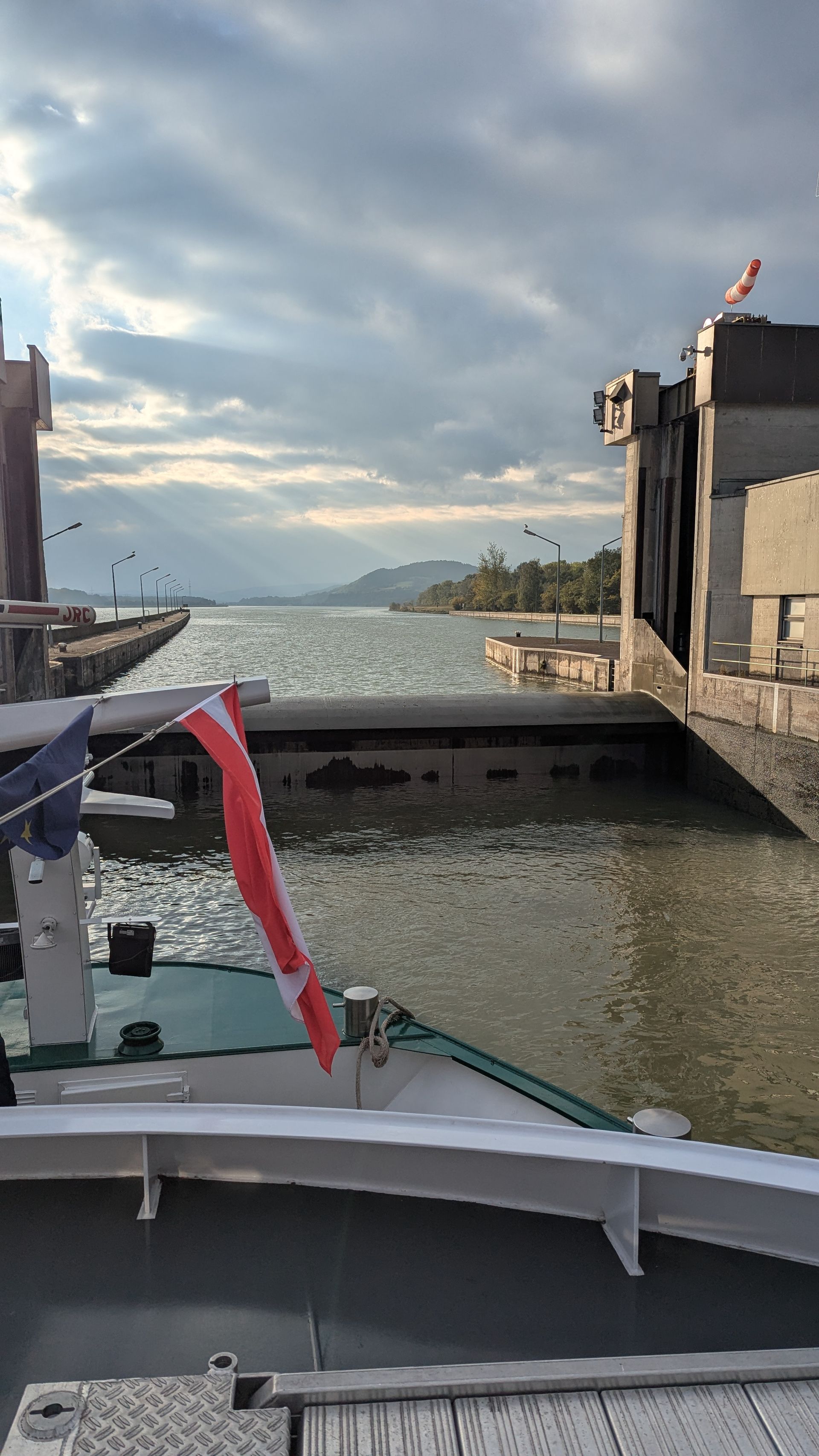 Boat passing through a lock, with a flag and cloudy sky. Water visible, distant shore.