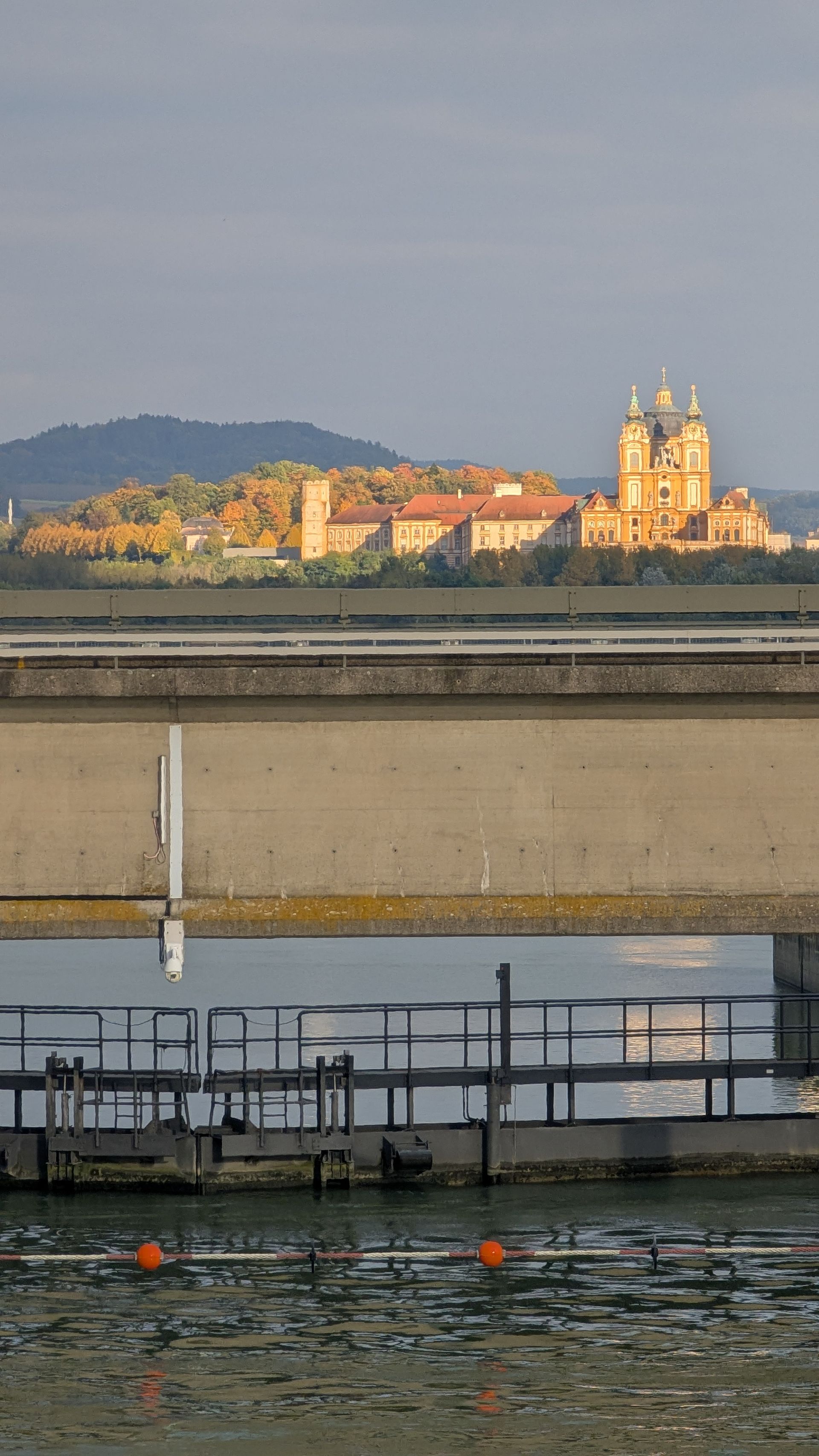 A large, ornate church building on a hill, seen across a body of water and a concrete structure.