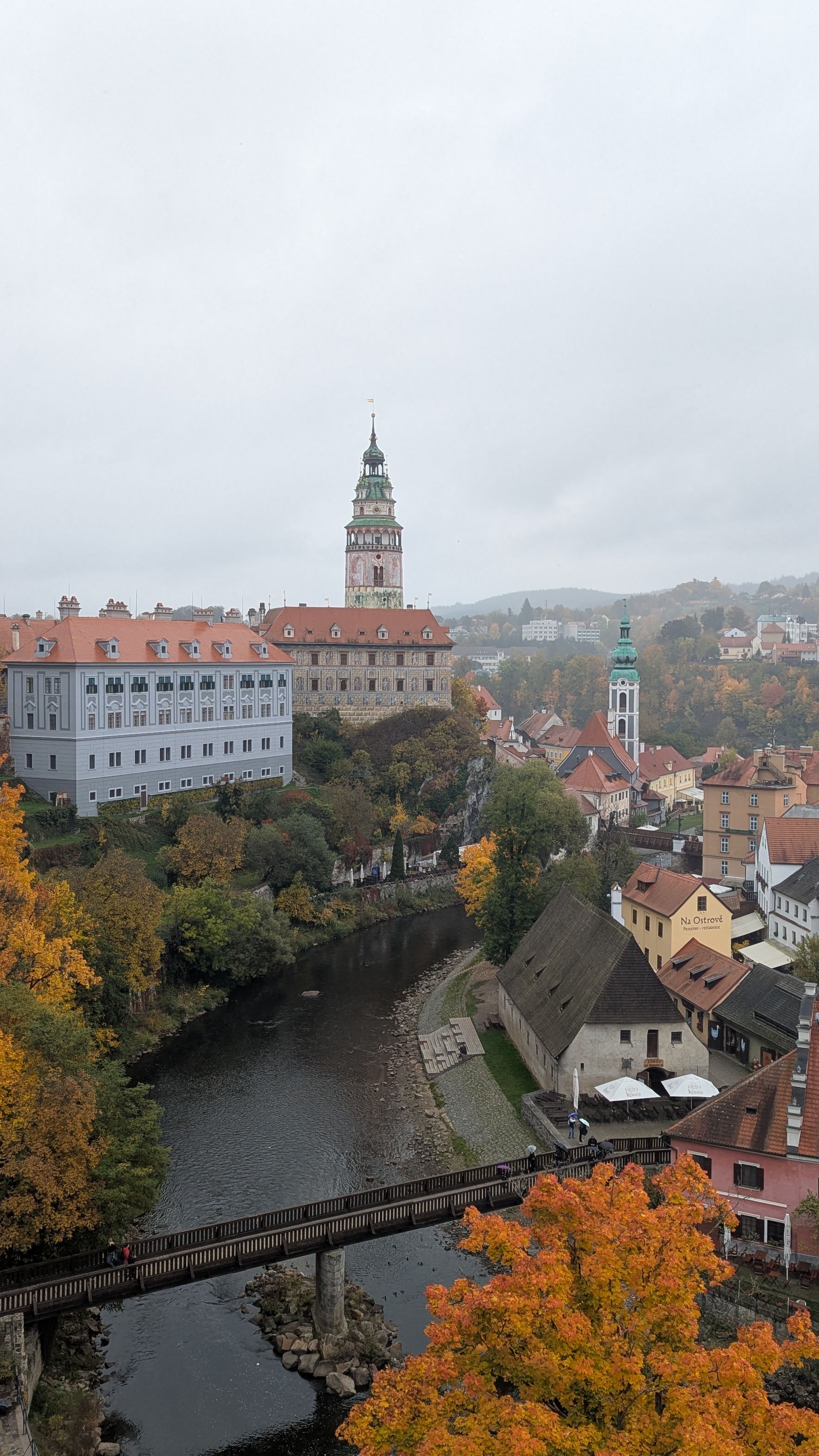 View of Cesky Krumlov, Czech Republic, buildings with orange autumn foliage and Vltava river under cloudy sky.