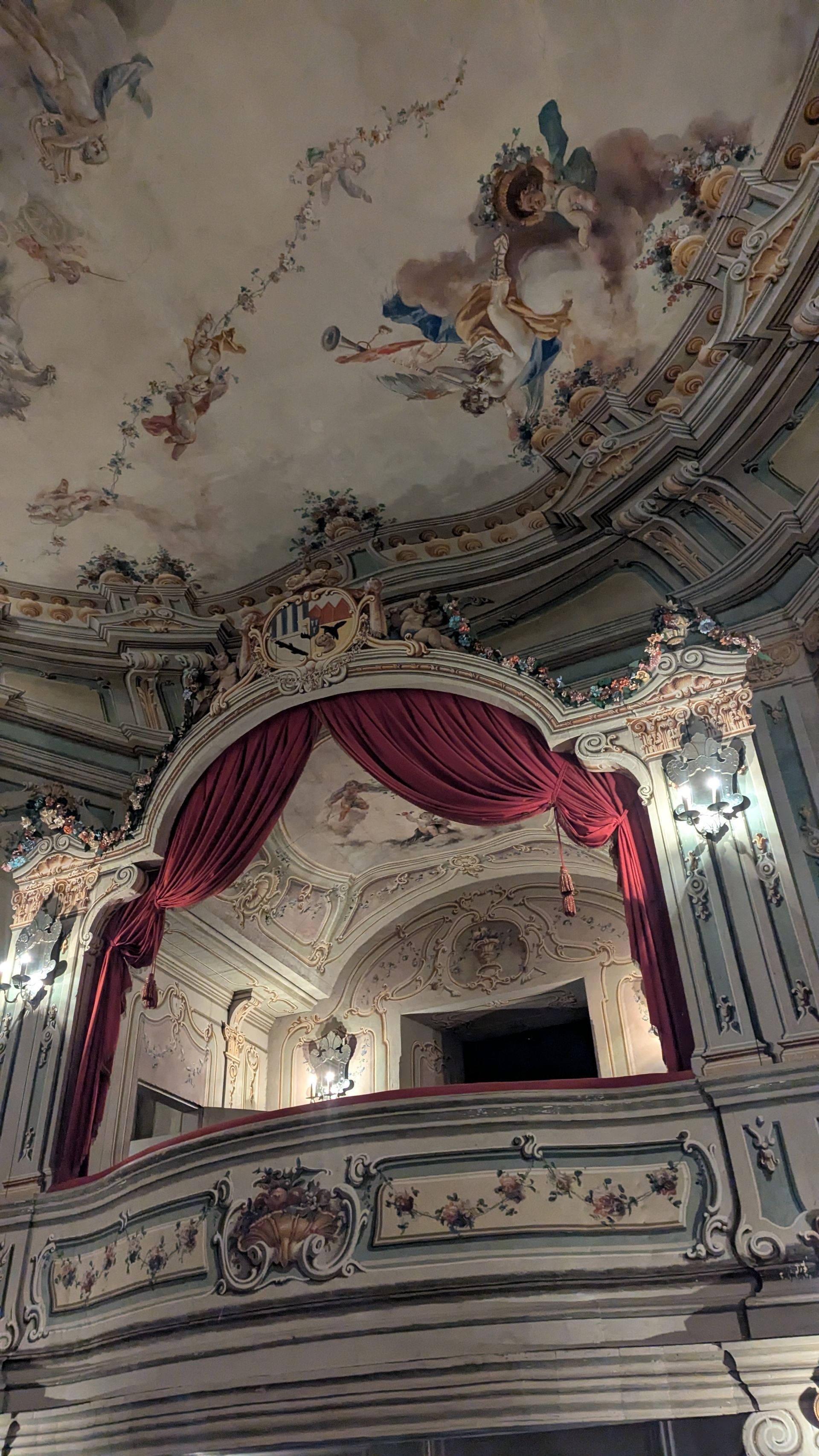 Ornate theater box with red curtain and ceiling fresco.