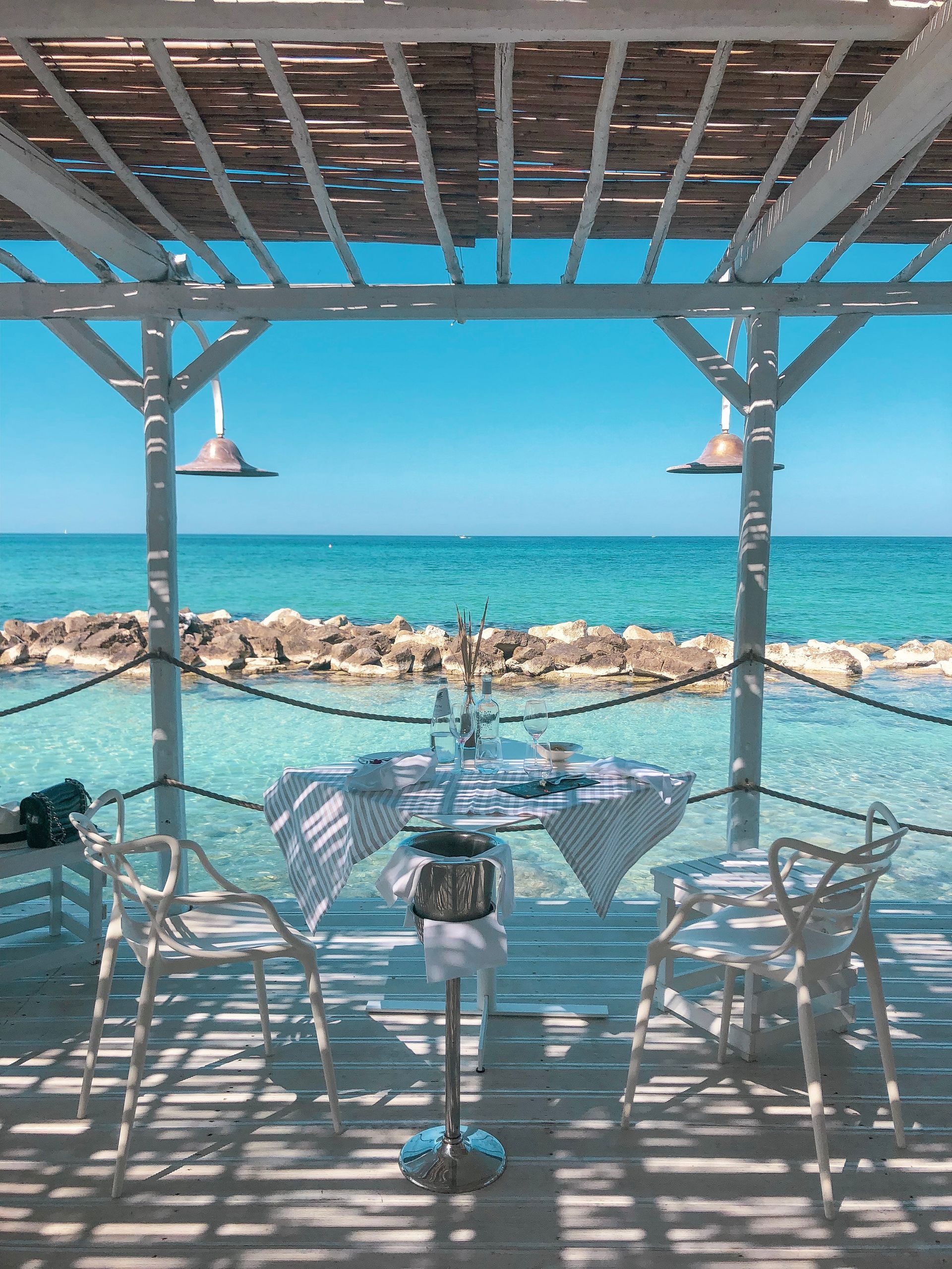 A table and chairs under a pergola overlooking the ocean at La Peschiera Hotel in Puglia, Italy.