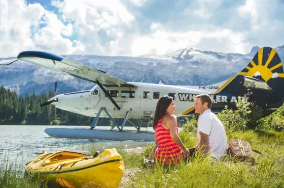 A man and a woman are sitting in the grass in front of a seaplane in Canada.