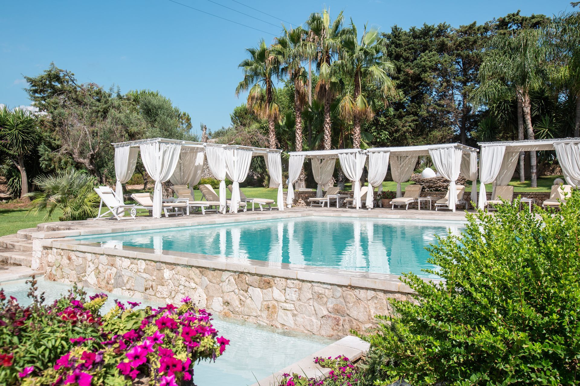 A large swimming pool surrounded by palm trees and flowers at Naturalis Bio Resort & Spa in Puglia, Italy.