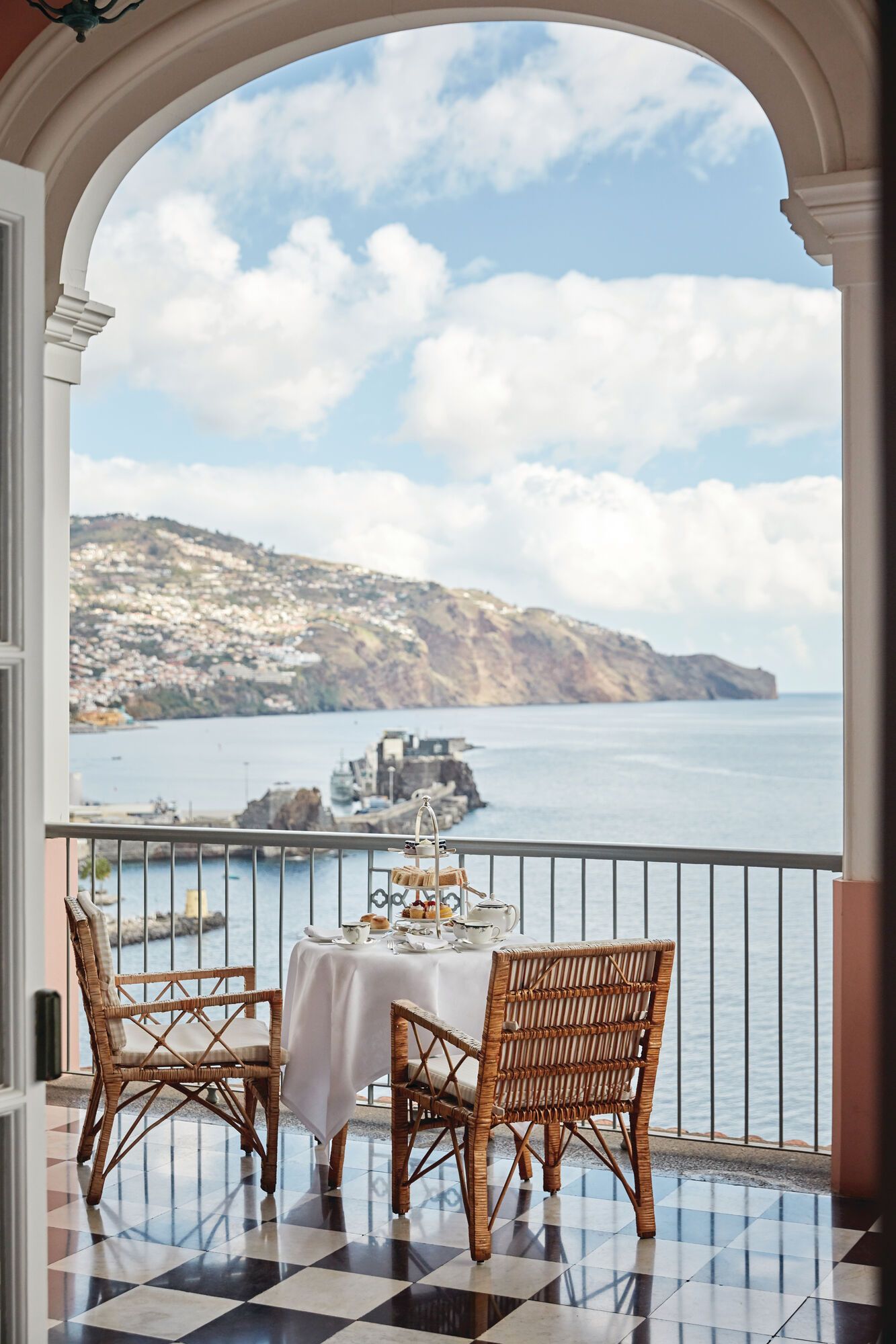 A balcony with a table and chairs overlooking the ocean in Madeira, Portugal at Belmond Hotel. 