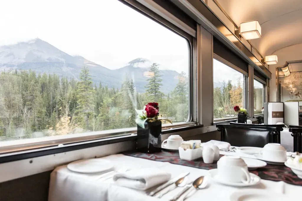 A dining room on a VIA Rail train with a view of mountains and trees.