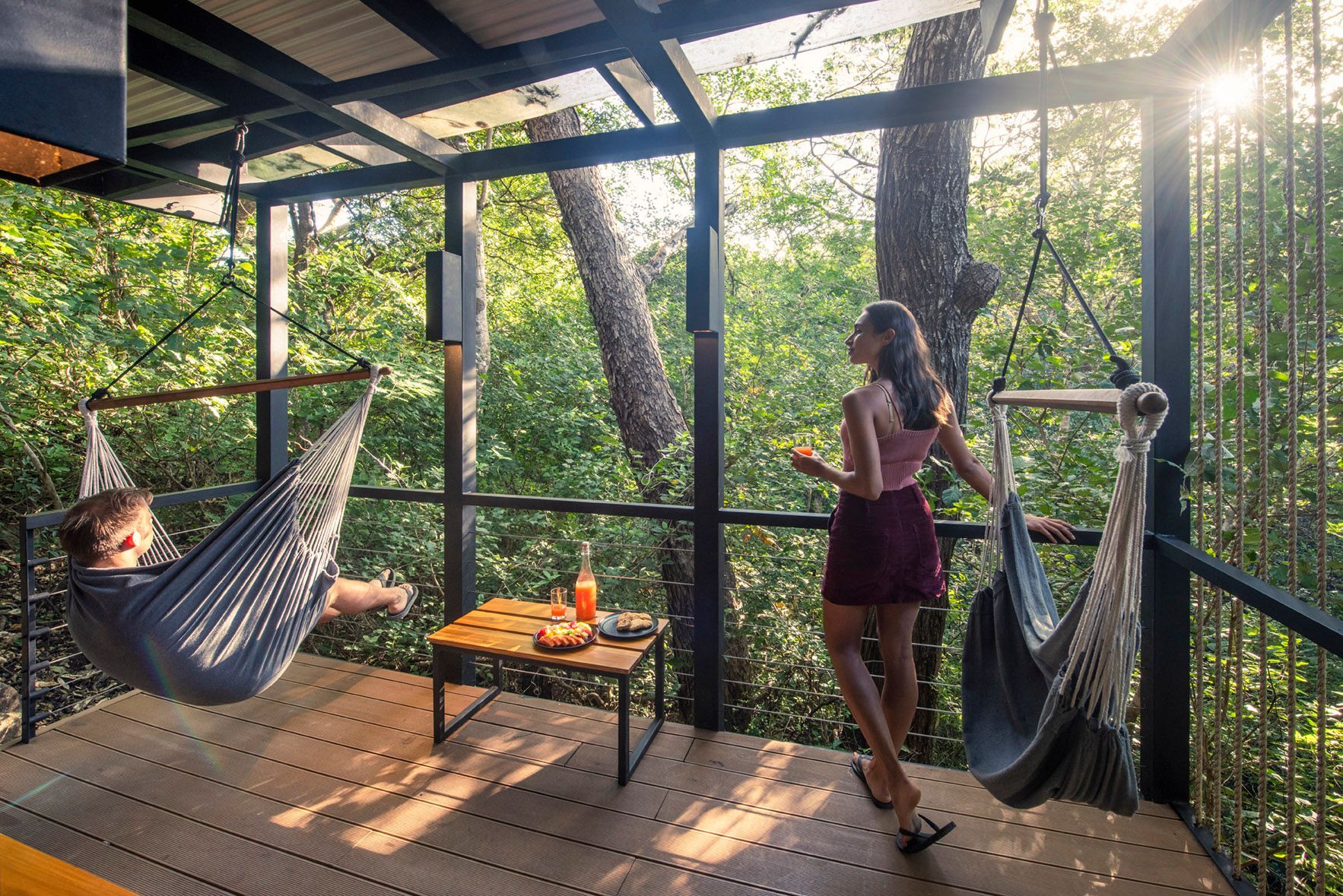 A woman is standing next to a man in a hammock on a deck in Costa Rica.