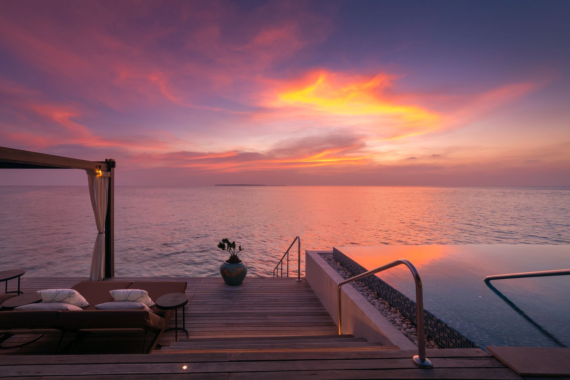 A sunset over the Maldives with a swimming pool in the foreground at velaa's overwater bungalow resort. 