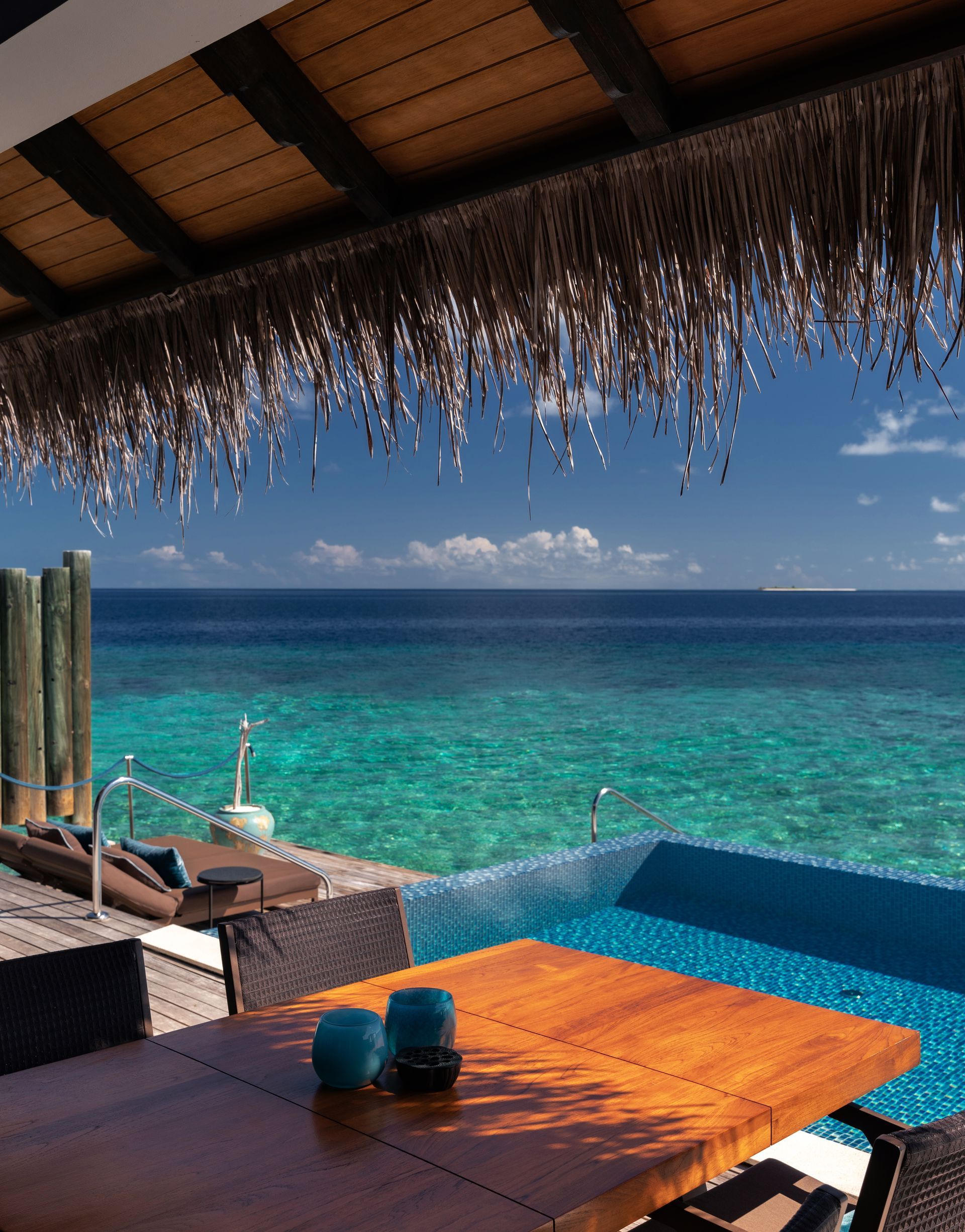 A table with candles on it sits next to a pool overlooking the Maldives at Velaa's overwater bungalow resort. 