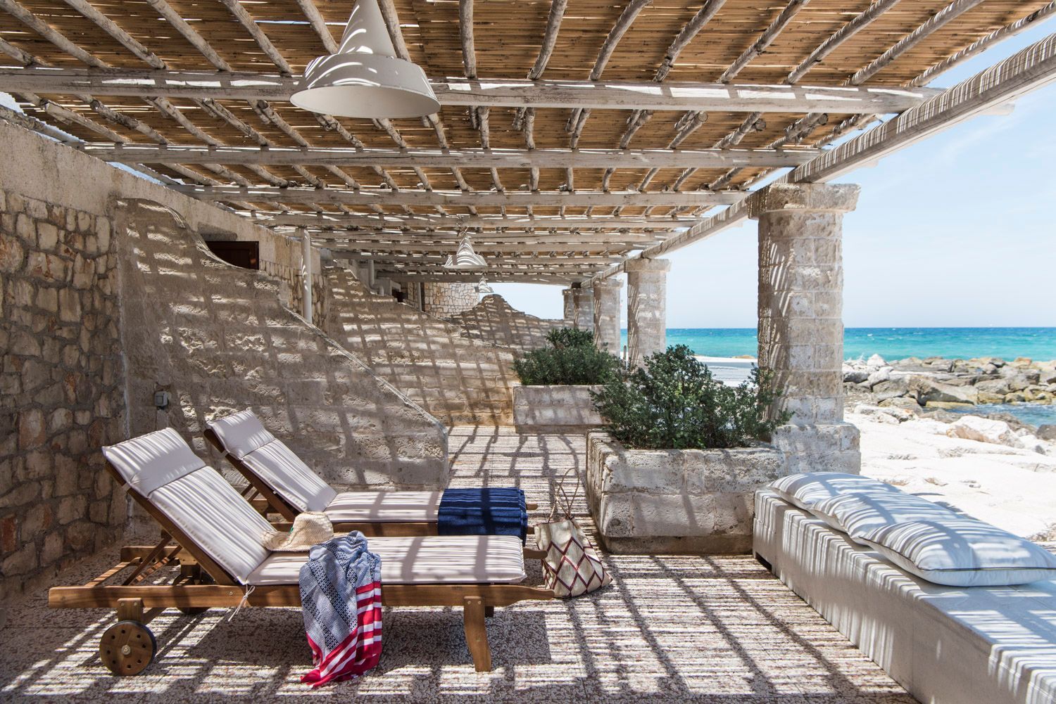 A patio with chairs under a pergola overlooking the ocean at La Peschiera Hotel in Puglia, Italy.