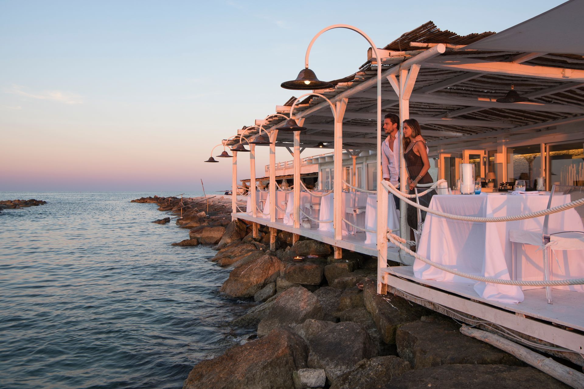 A couple standing on a pier overlooking the ocean at La Peschiera Hotel in Puglia, Italy.