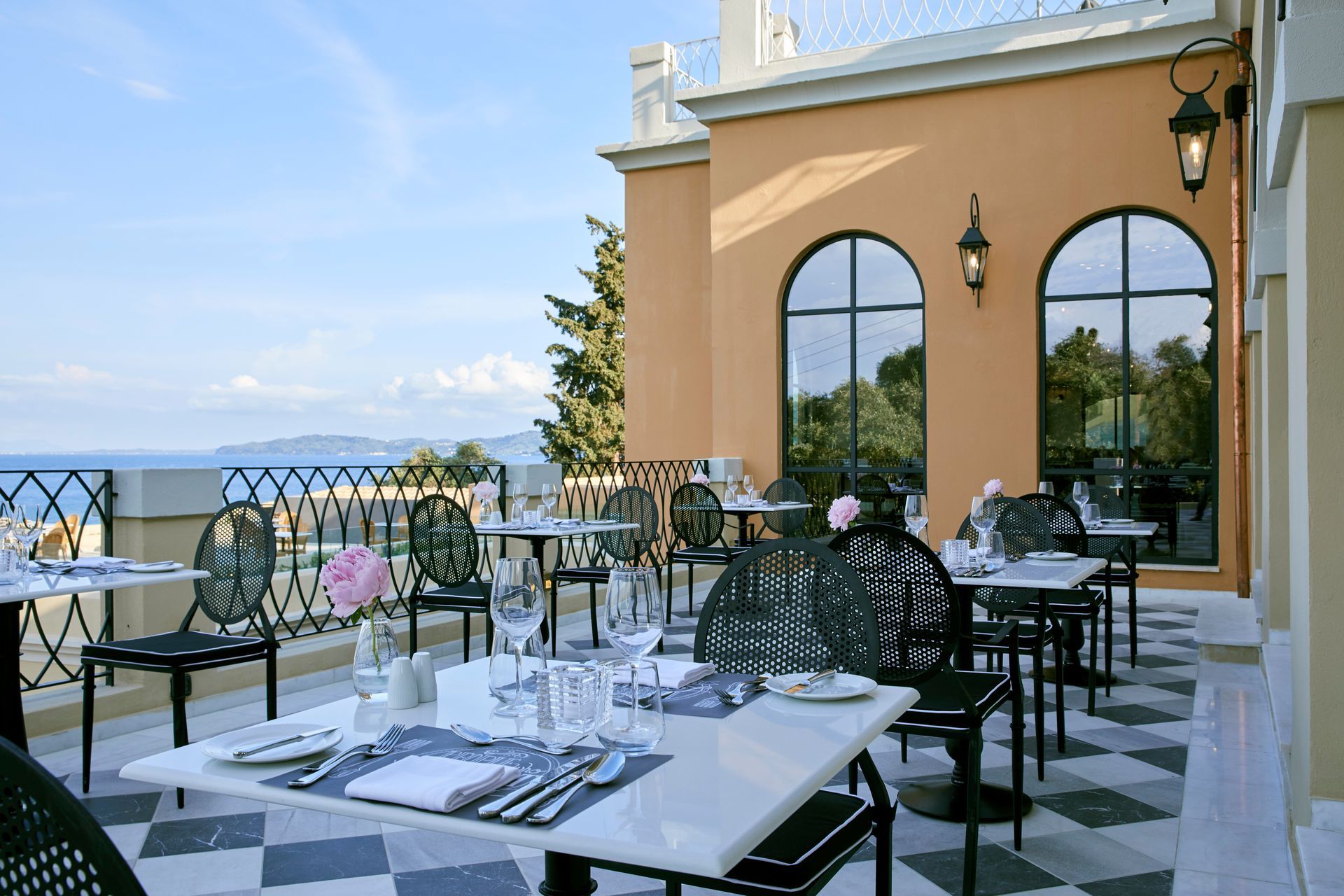 A patio with tables and chairs and a view of the ocean at Nido Hotel, Mar-Bella Collection in Corfu, Greece.