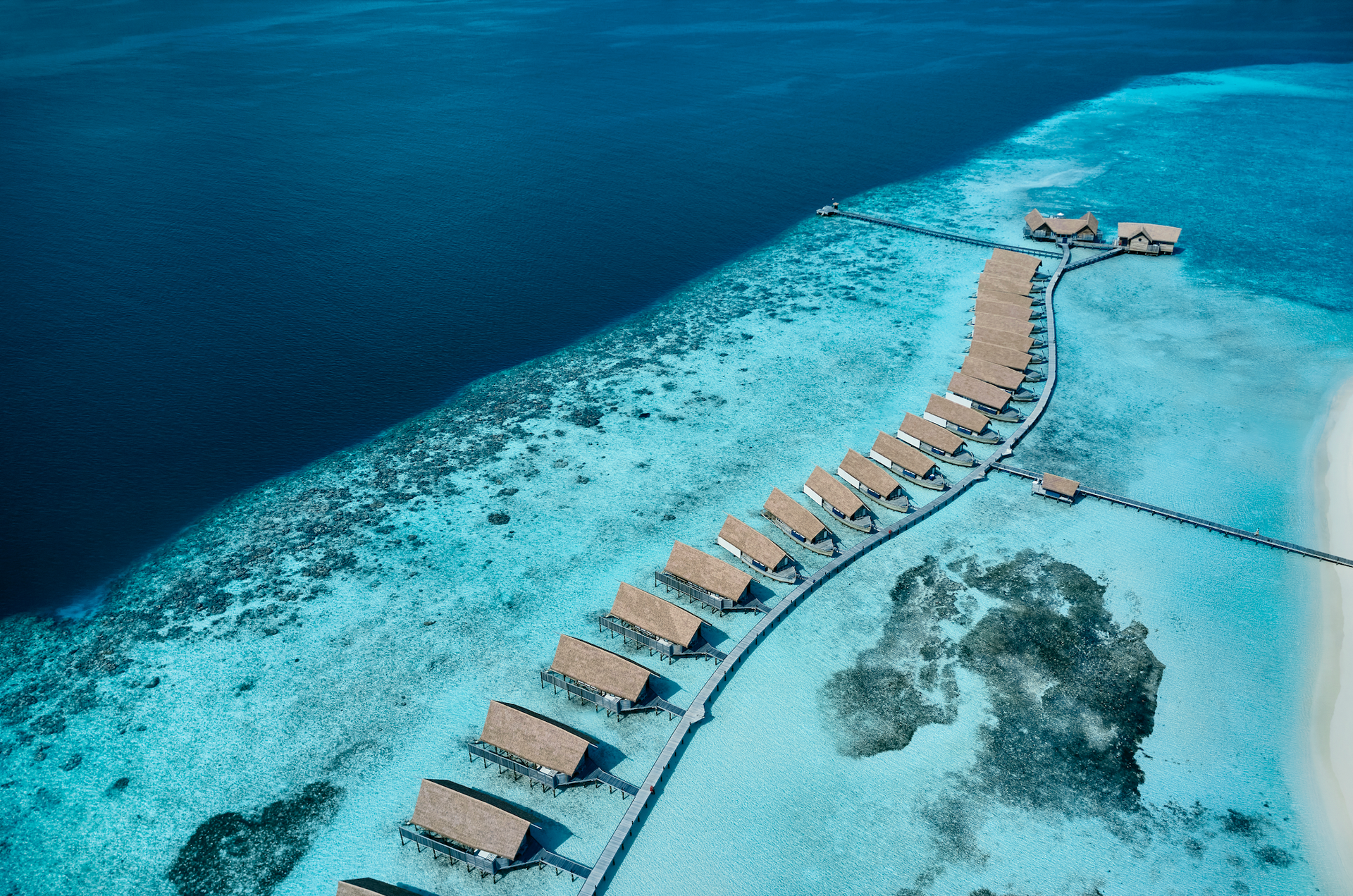 An aerial view of the Maldives with a strip of COMOs over the water bungalows. 