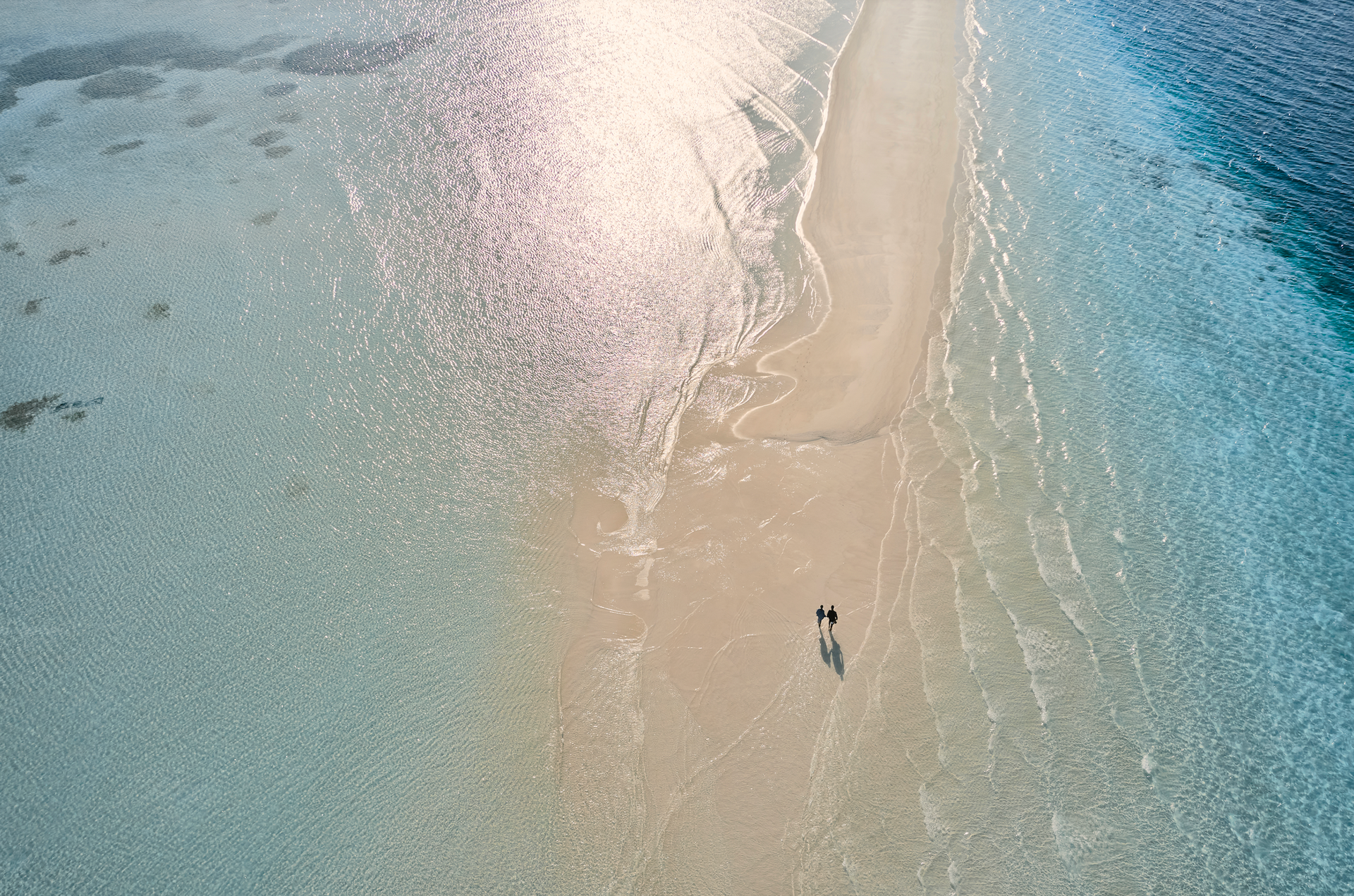 An aerial view of a couple walking on a sandy beach in the Maldives at como resort. 