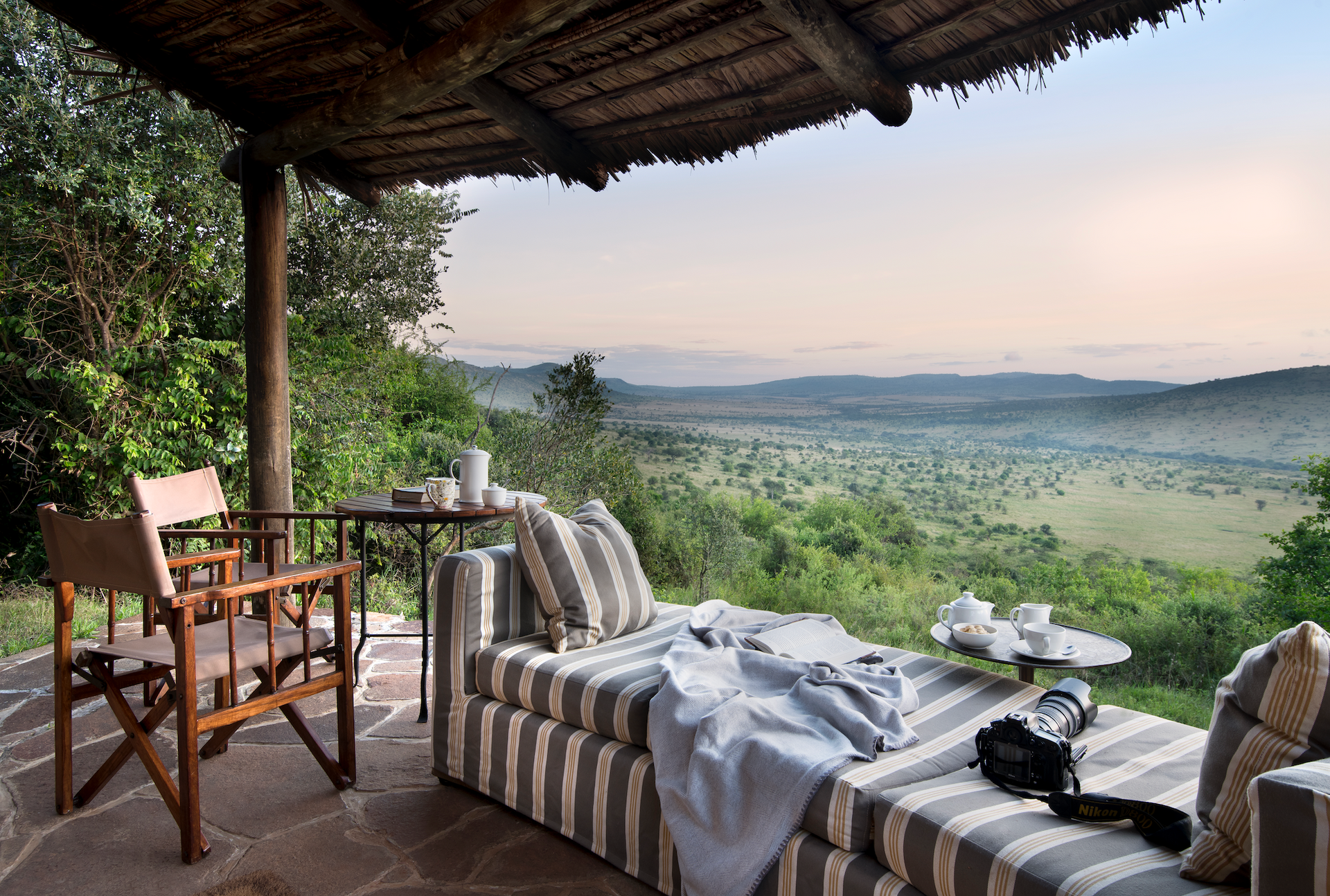 A patio with a couch and chairs overlooking a lush green field at a lodge in Africa.