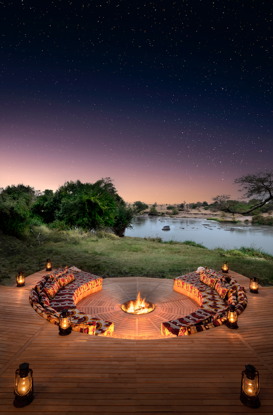 A group of people are sitting around a fire pit in the middle of a field at a camp in Africa.