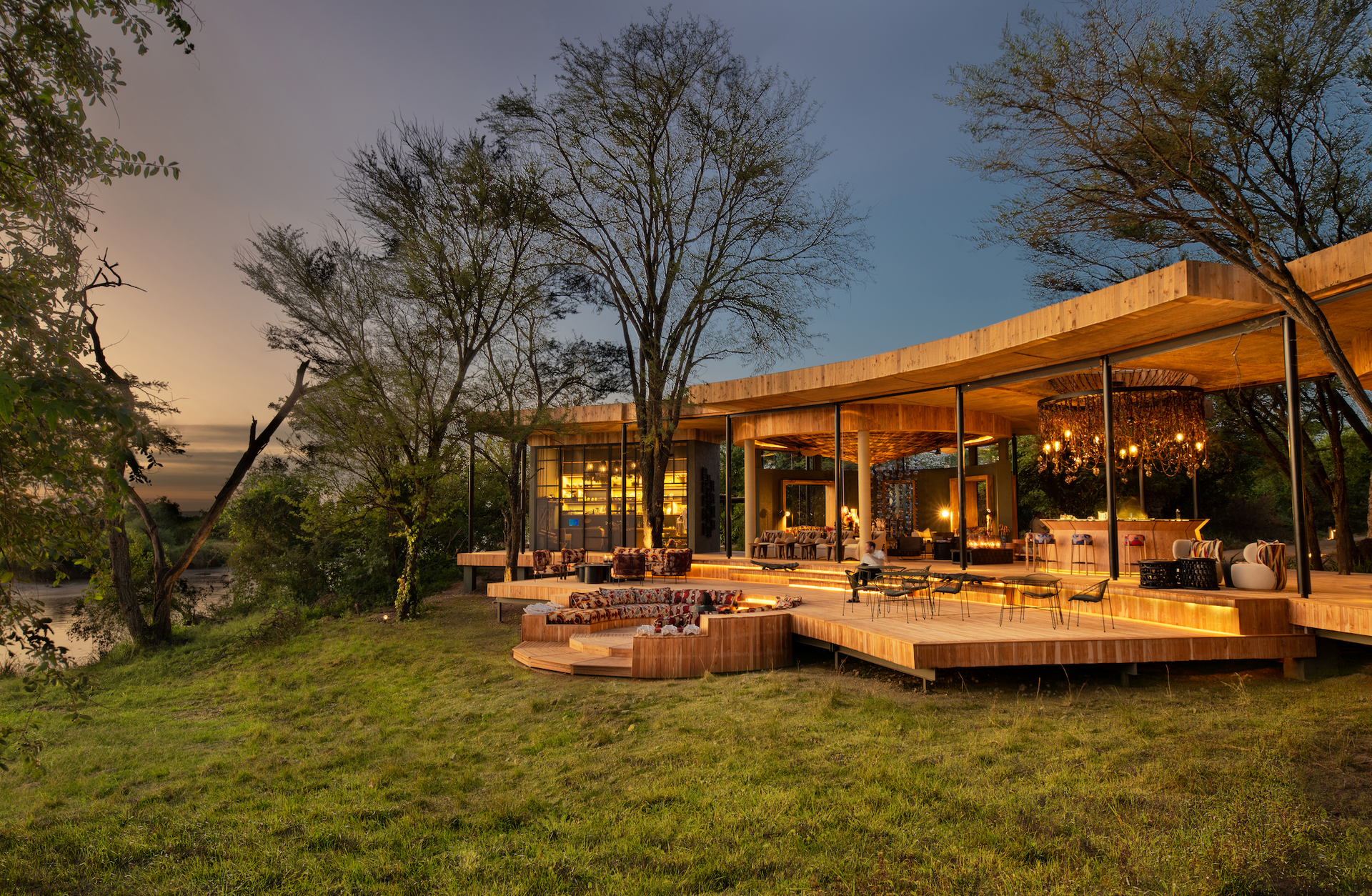 A large lodge with a lot of windows is surrounded by trees and grass in Africa.